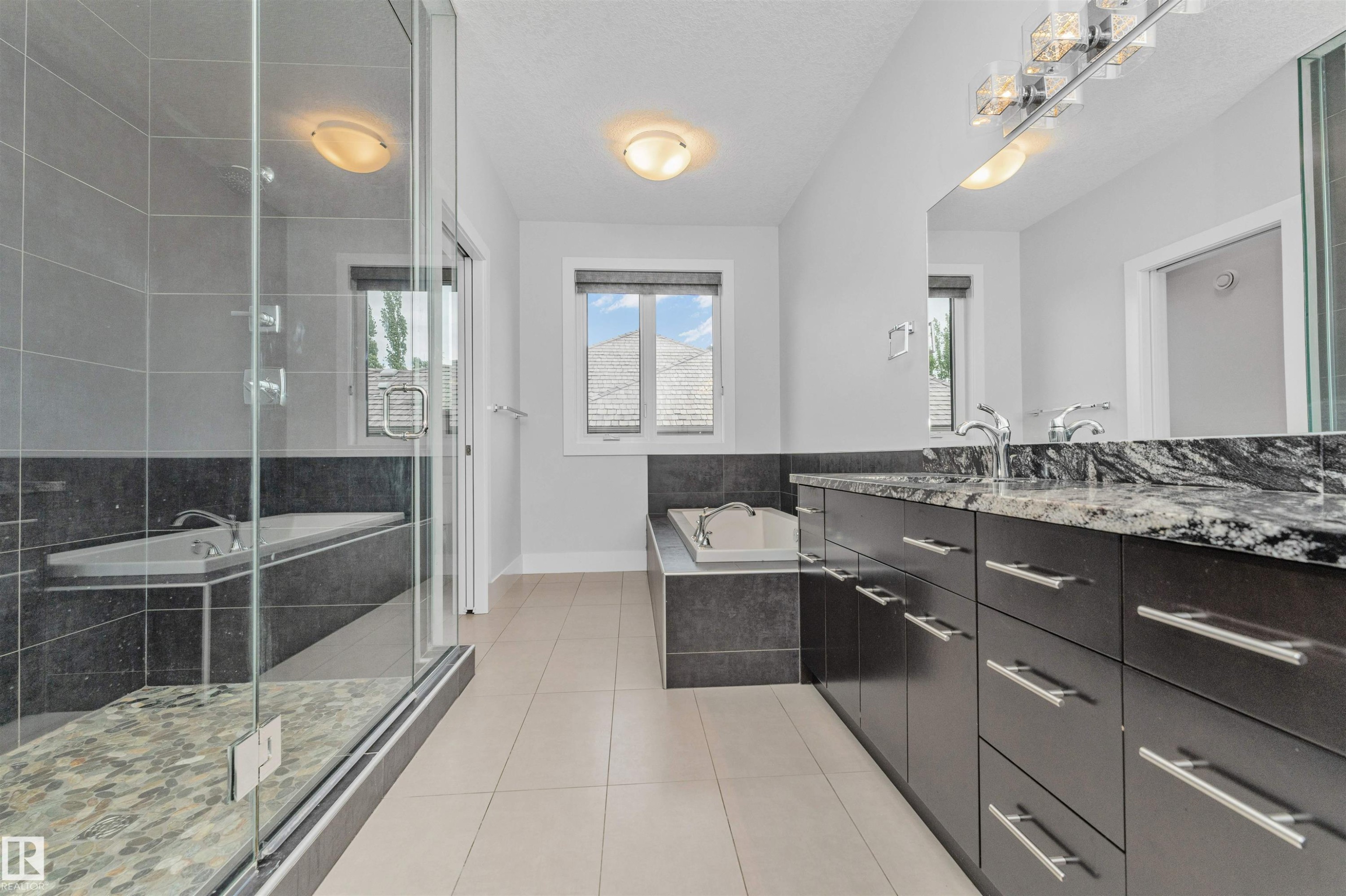 Spacious bathroom featuring a frameless glass shower enclosure, a built-in soaking tub, a dual vanity with a patterned countertop, dark wood-finish cabinetry, and chrome fixtures - 3310 Watson Bay, Edmonton, AB