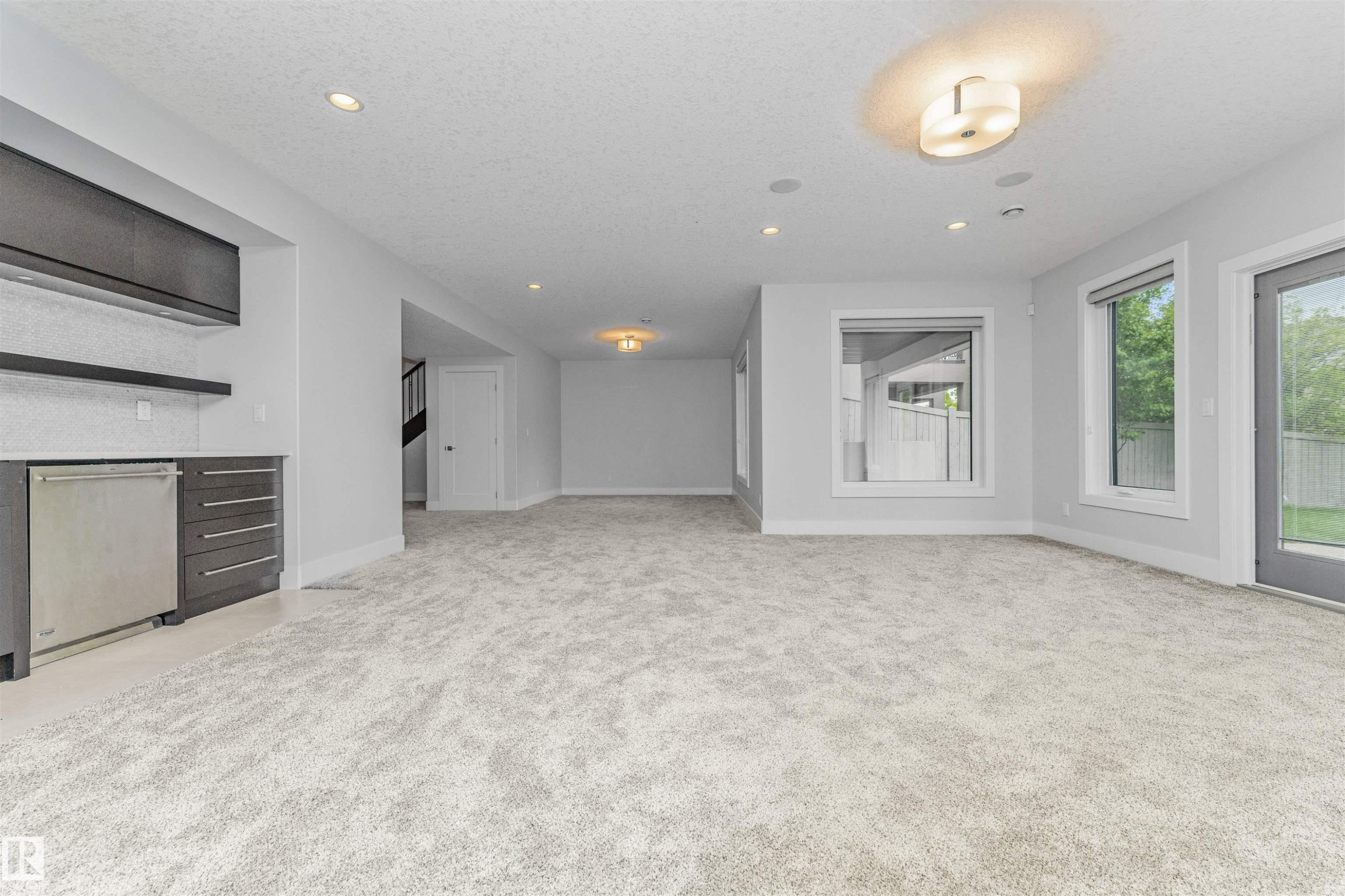 Spacious room featuring new carpeting, recessed lighting, and a built-in wet bar with dark wood-finish cabinetry and a stainless steel undercounter appliance - 3310 Watson Bay, Edmonton, AB
