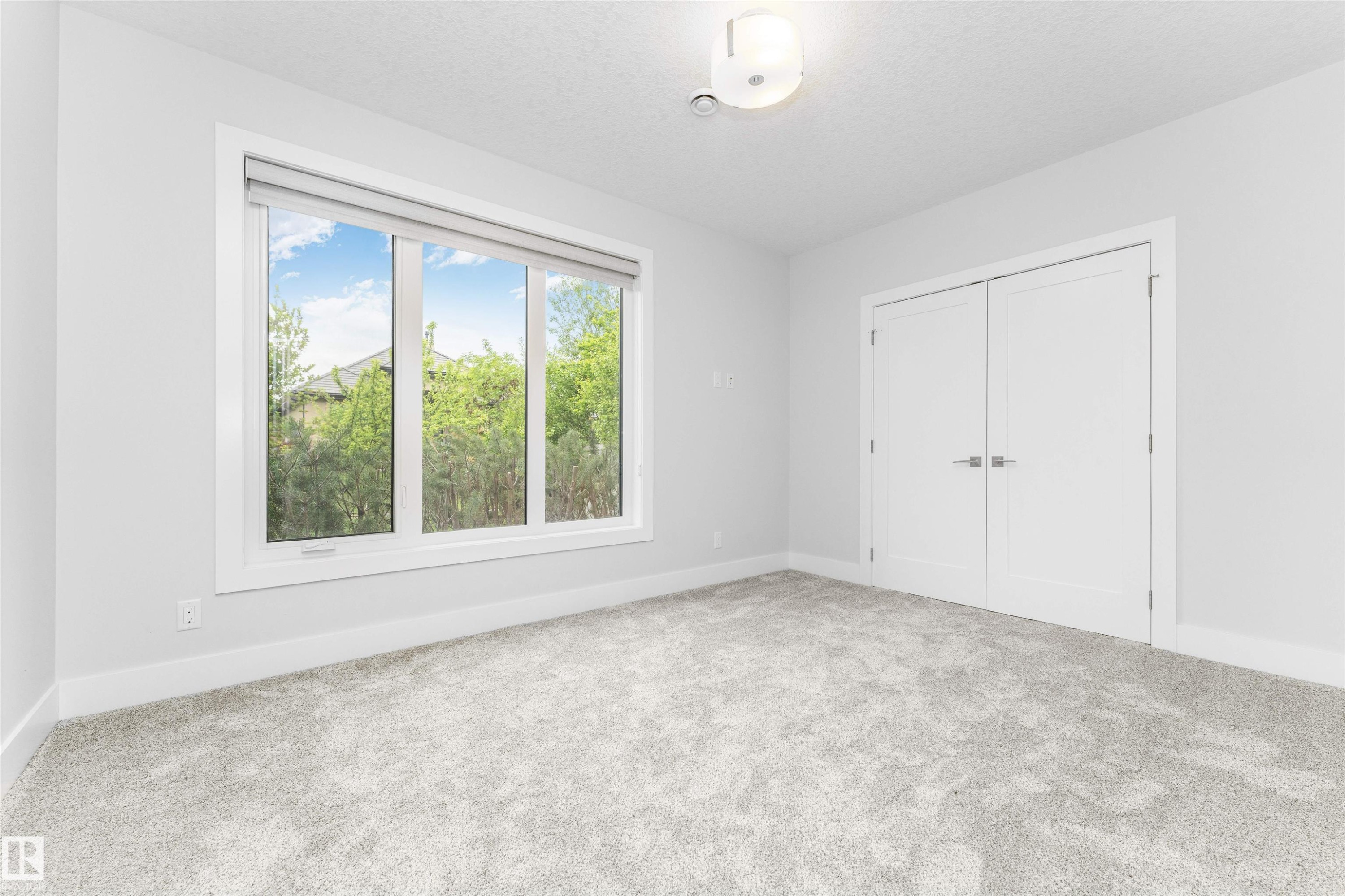 Bright interior space featuring a large three-panel window with roller shades, light grey carpet, white trim, and double white doors with modern hardware - 3310 Watson Bay, Edmonton, AB