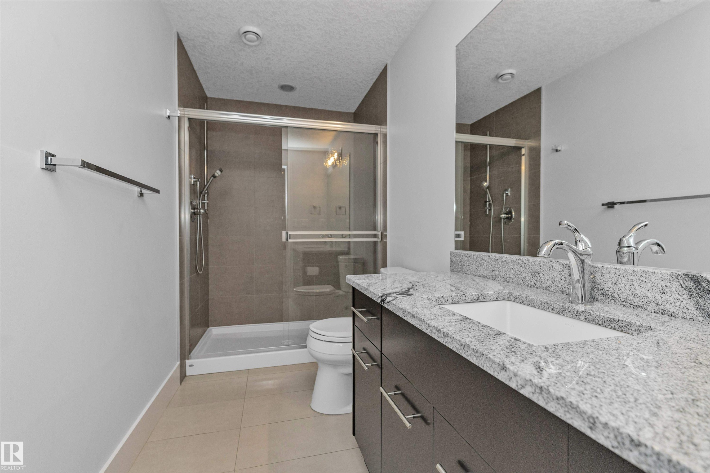 Bathroom featuring a spacious walk-in shower with glass enclosure, a vanity with a light-toned granite countertop, dual undermount sinks, and a large mirror - 3310 Watson Bay, Edmonton, AB