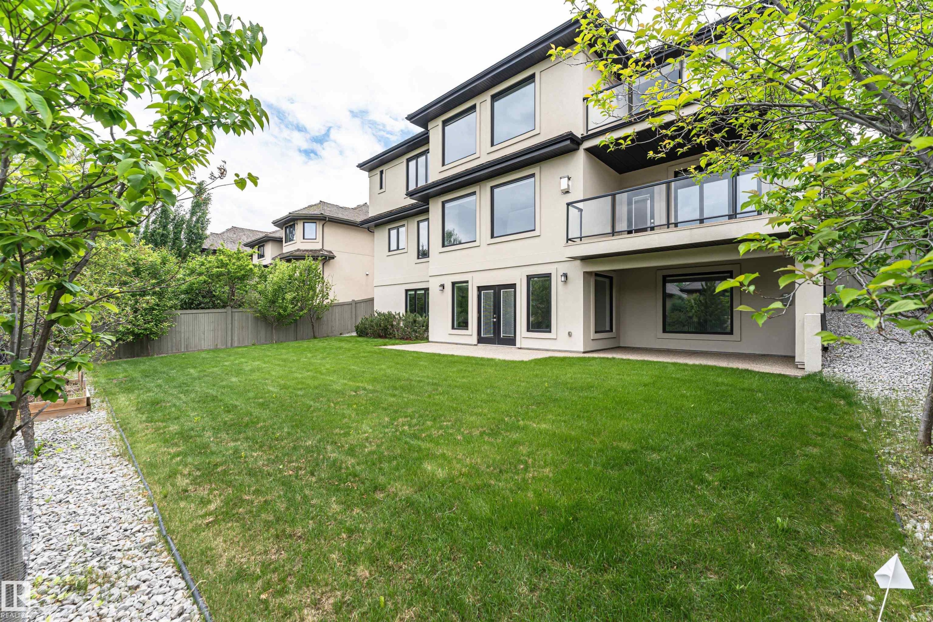 Stucco exterior featuring a ground-level patio, second-story balcony with glass railings, and expansive windows - 3310 Watson Bay, Edmonton, AB