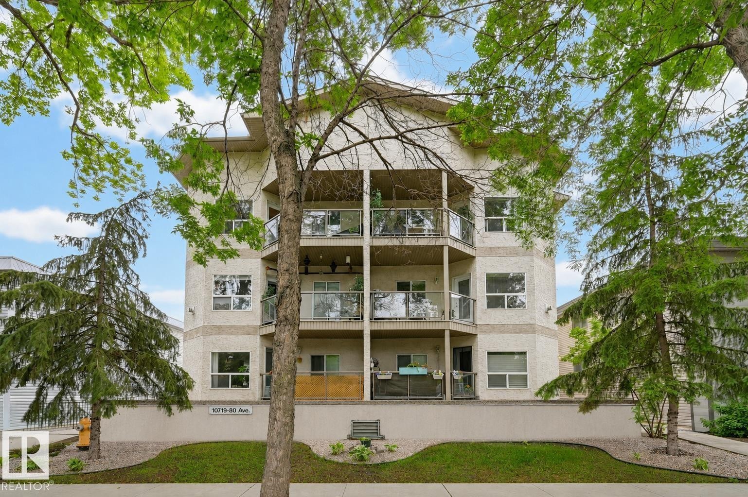 Multi-story building featuring stucco exterior and multiple balconies with glass railings - 203 10719 80 Avenue, Edmonton, AB