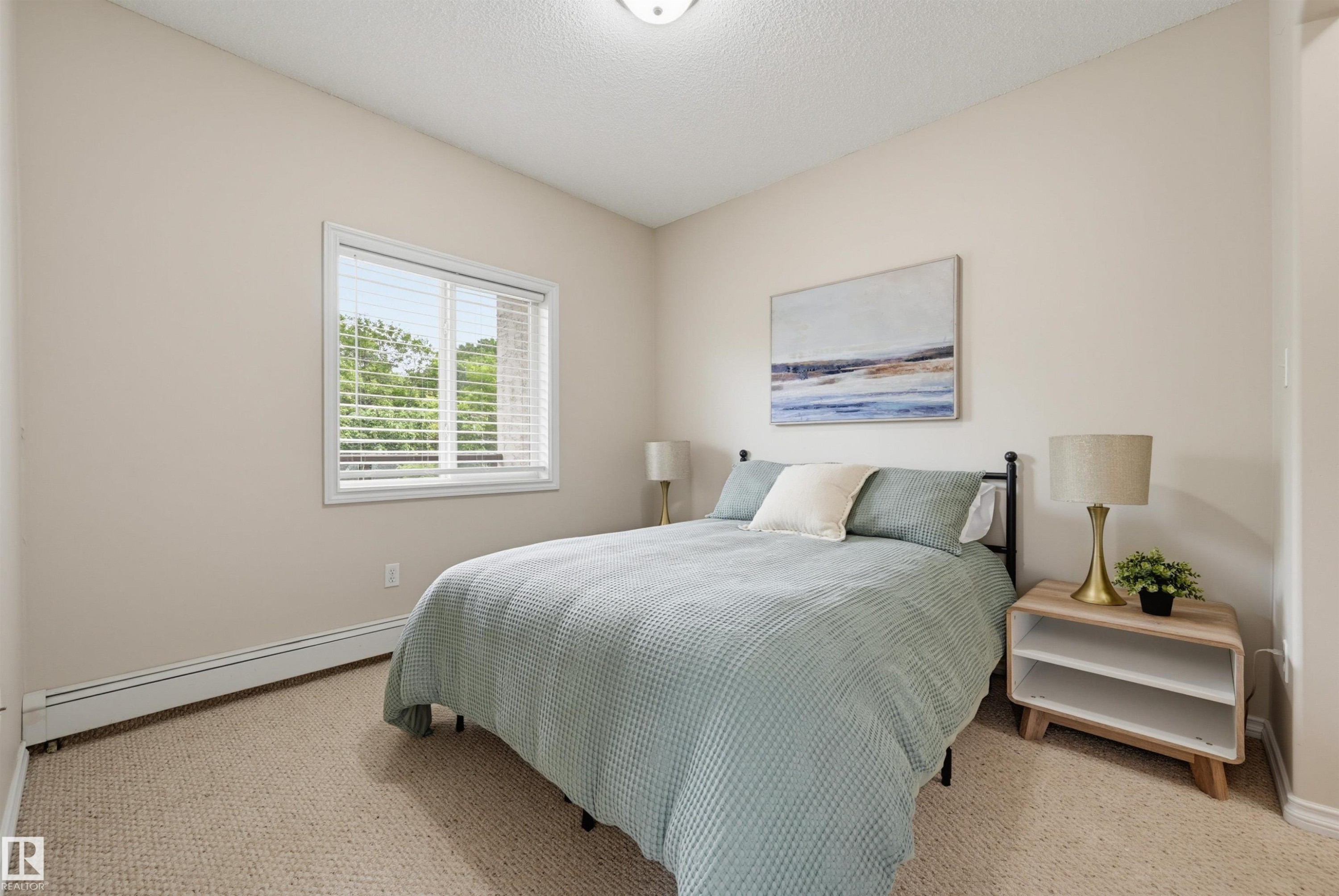 Carpeted room with a large window featuring horizontal blinds - 203 10719 80 Avenue, Edmonton, AB