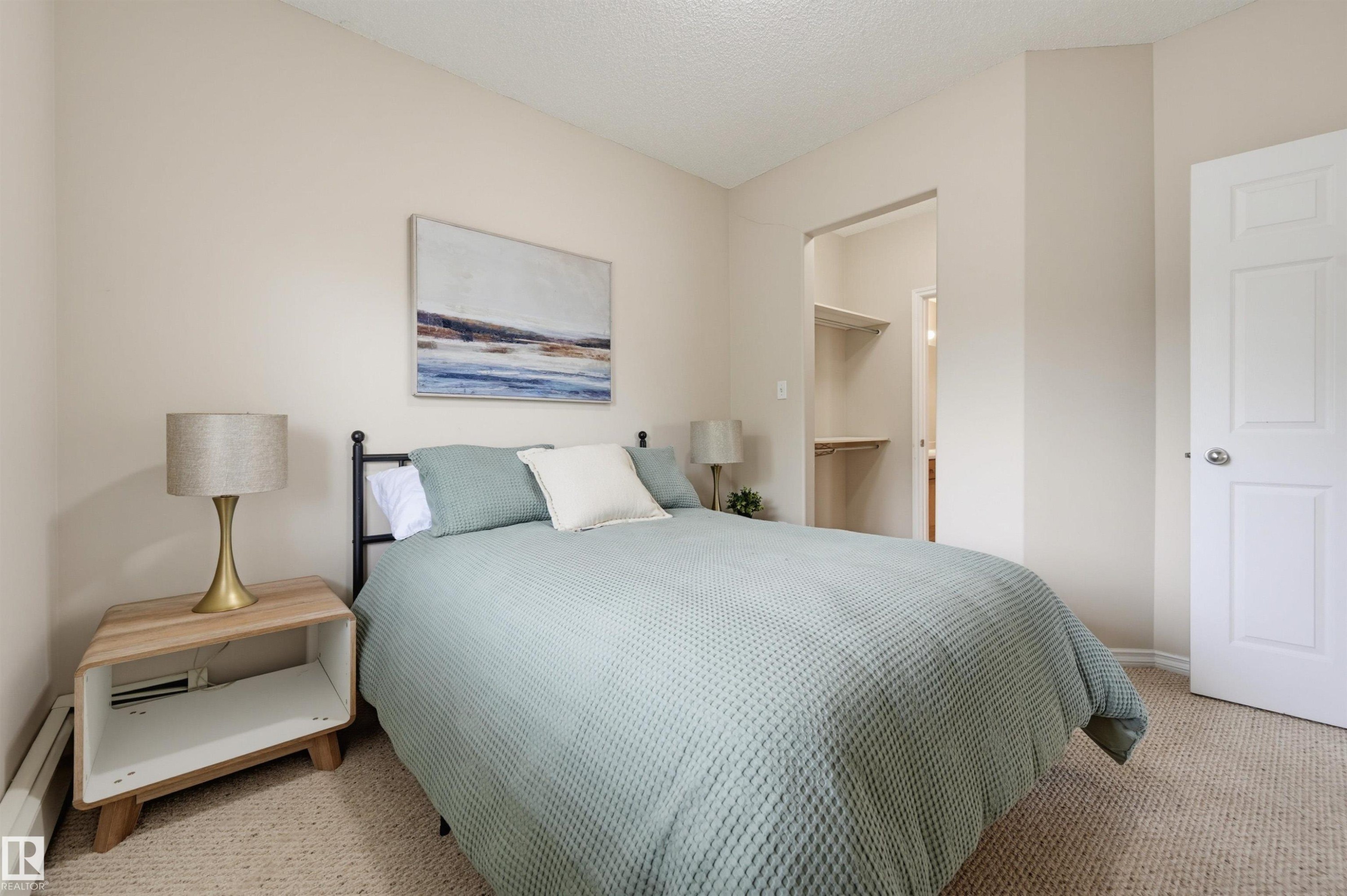 Wall-to-wall carpeting with light-toned walls, featuring a closet alcove with built-in shelving, a white paneled door, and baseboard trim - 203 10719 80 Avenue, Edmonton, AB