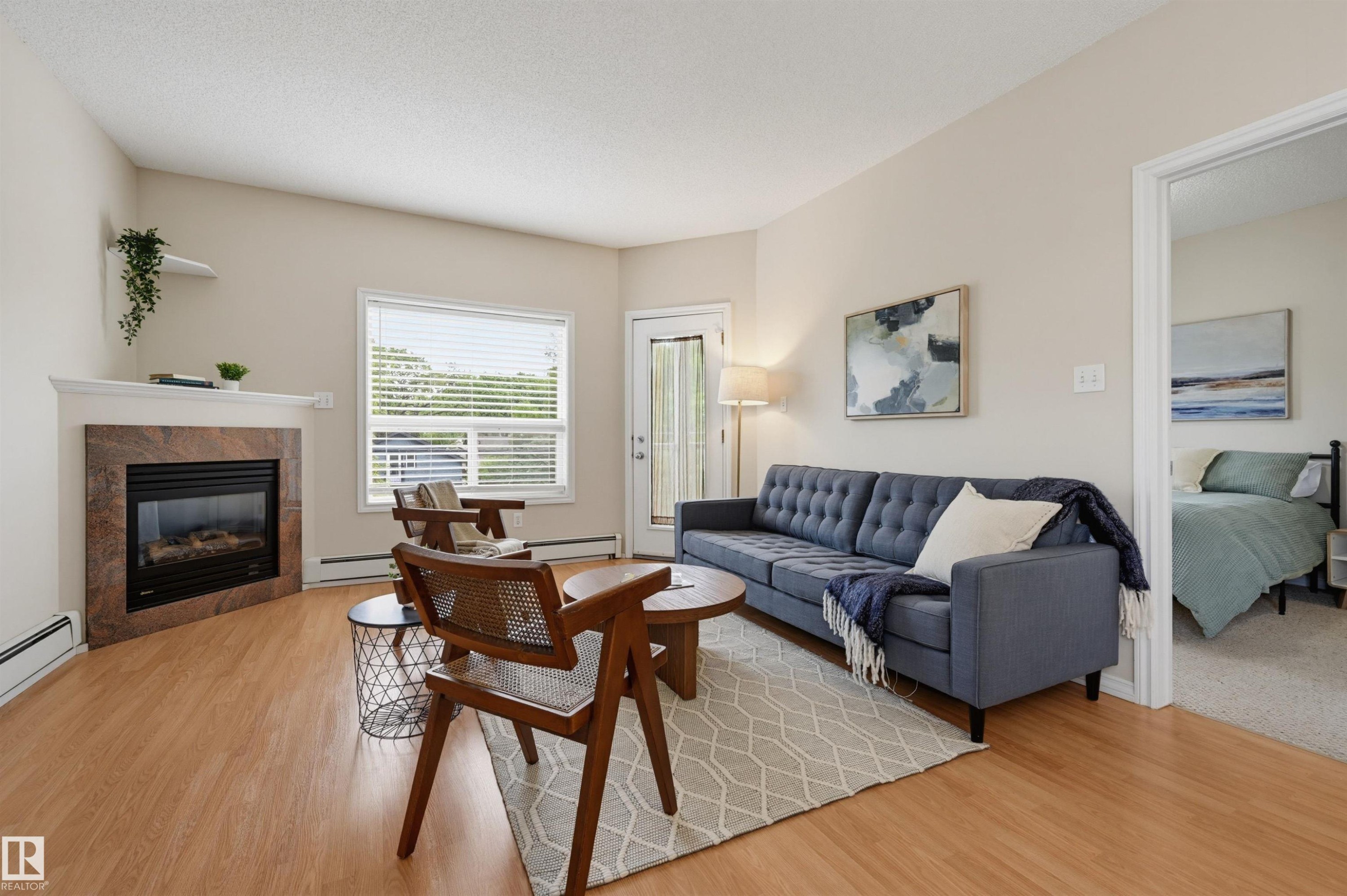 Living area featuring wood-finish flooring, a corner fireplace with a stone surround, and a white mantel - 203 10719 80 Avenue, Edmonton, AB