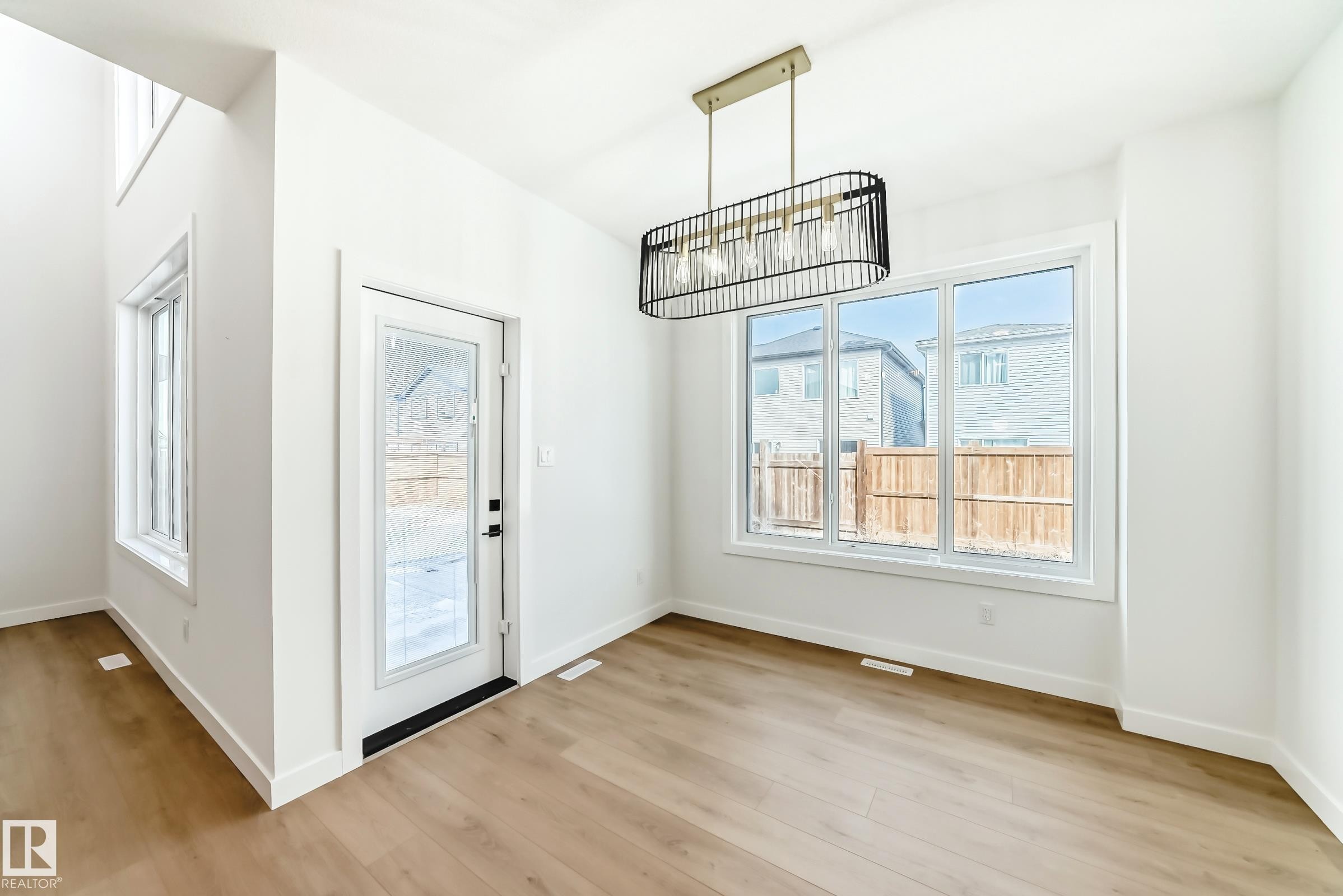 Bright interior space featuring wood-finish flooring, white trim, and a modern linear chandelier - 341 Roberts Wynd, Leduc, AB