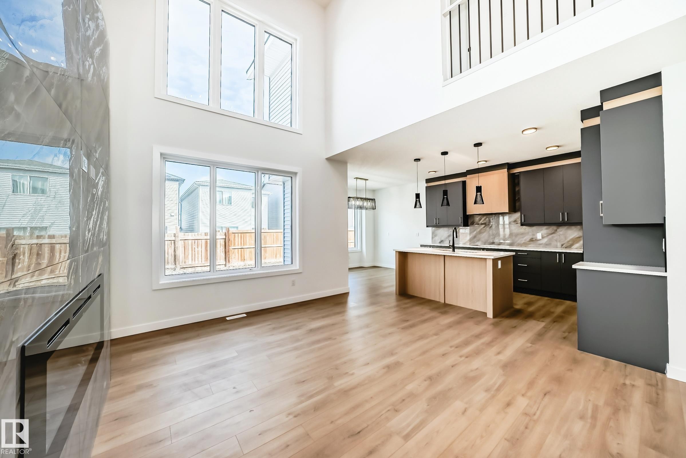Open-concept living space featuring wood-finish flooring, a two-story ceiling, and a contemporary fireplace with a large format tile surround - 341 Roberts Wynd, Leduc, AB