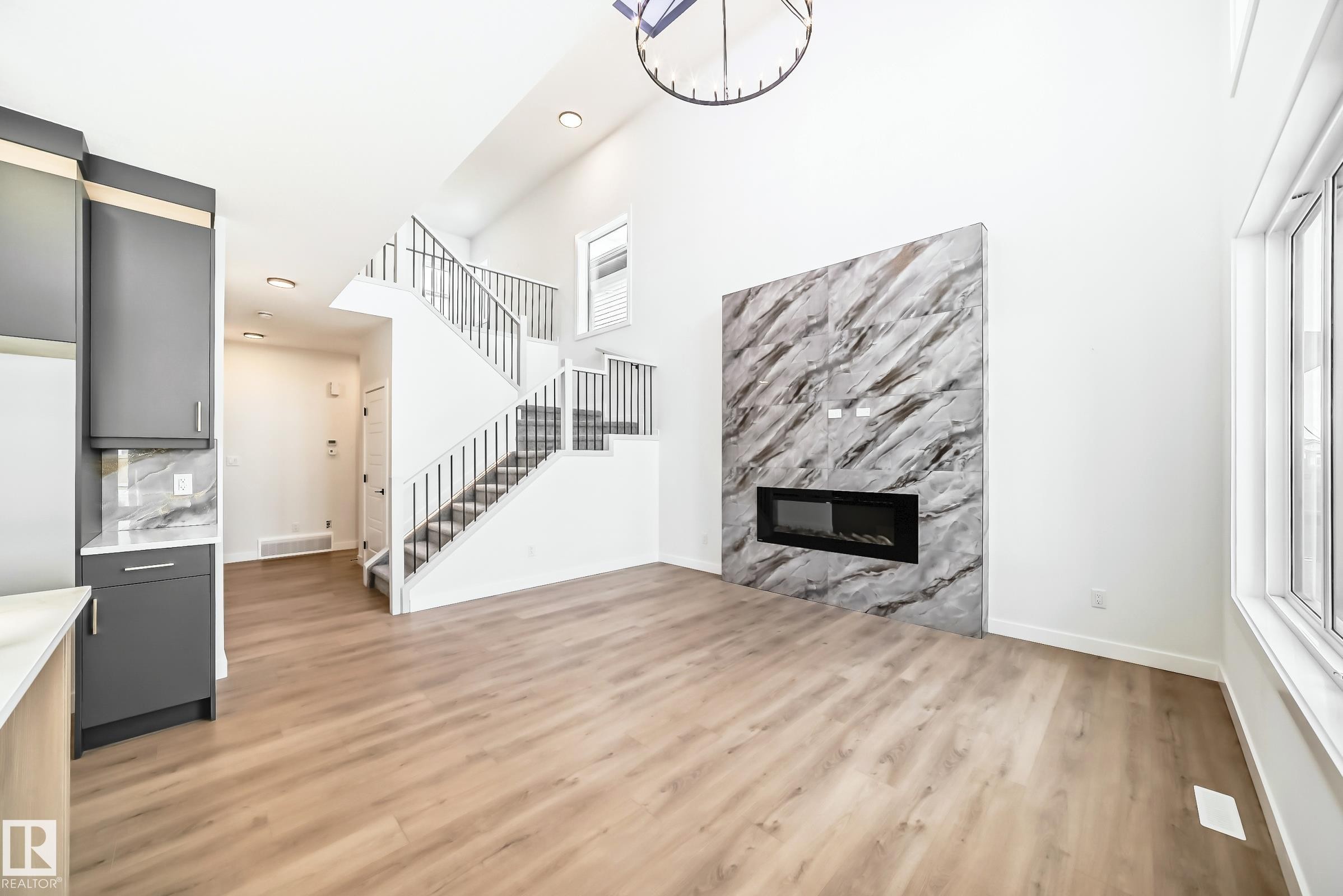 Expansive living space featuring high ceilings, wood-finish flooring, and a modern electric fireplace with a large format tile surround - 341 Roberts Wynd, Leduc, AB