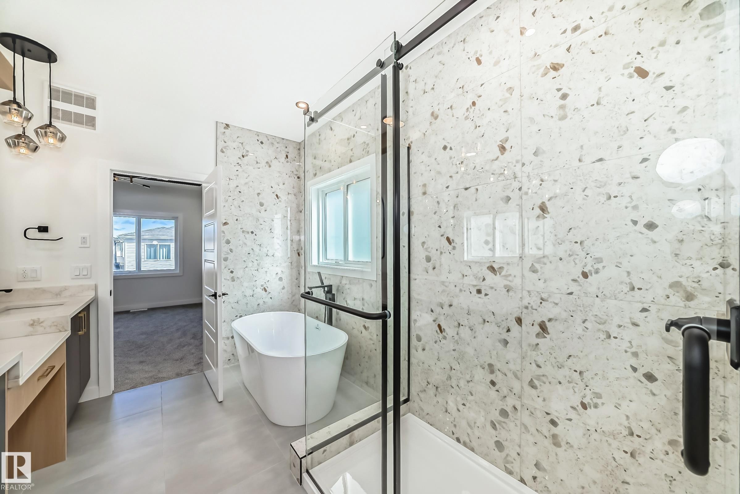 Contemporary bathroom featuring a freestanding soaking tub, glass-enclosed shower with black hardware, and speckled wall tile - 341 Roberts Wynd, Leduc, AB