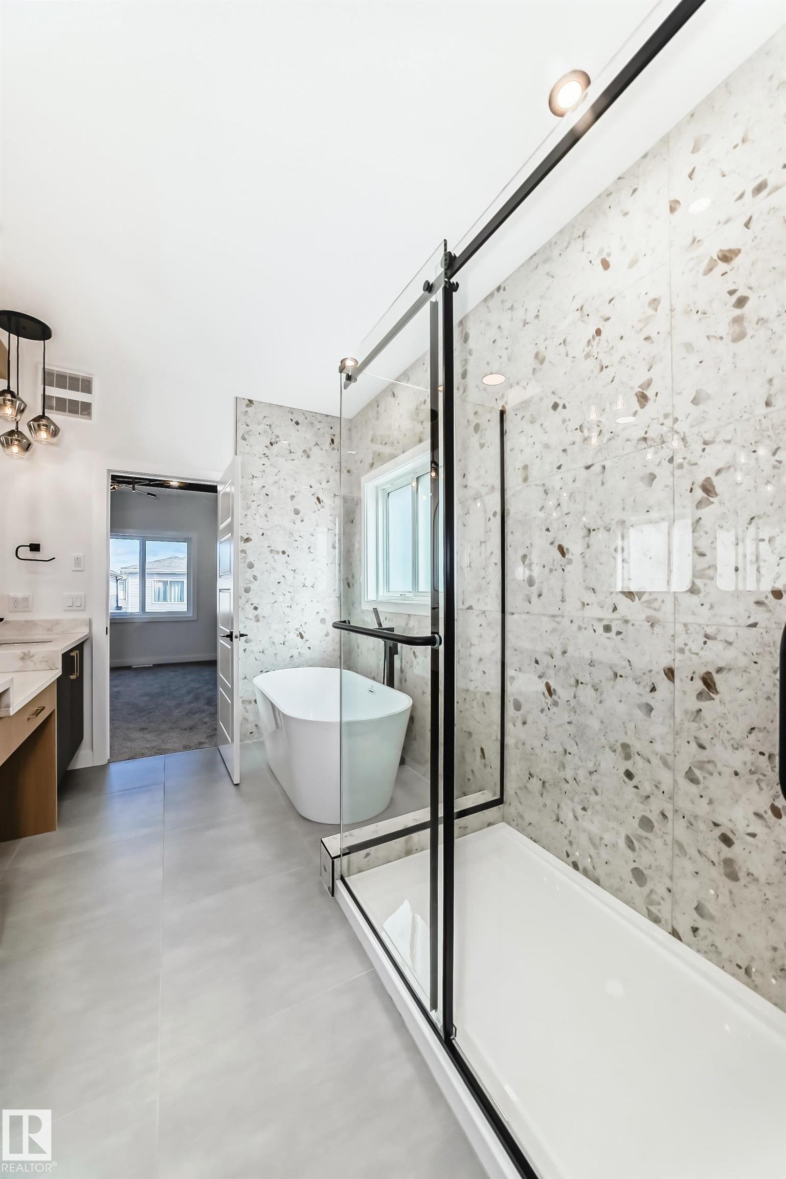 Contemporary bathroom featuring a freestanding tub, a walk-in shower with a glass enclosure, terrazzo-style tile walls, and large format floor tiles - 341 Roberts Wynd, Leduc, AB