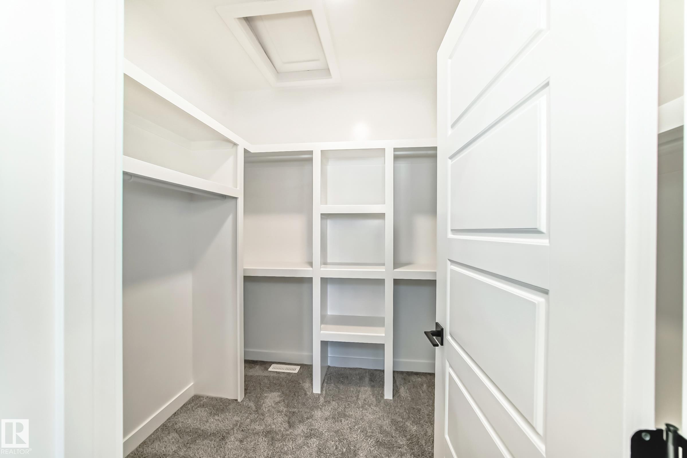 Walk-in closet featuring white built-in shelving, hanging rods, and gray carpet flooring - 341 Roberts Wynd, Leduc, AB