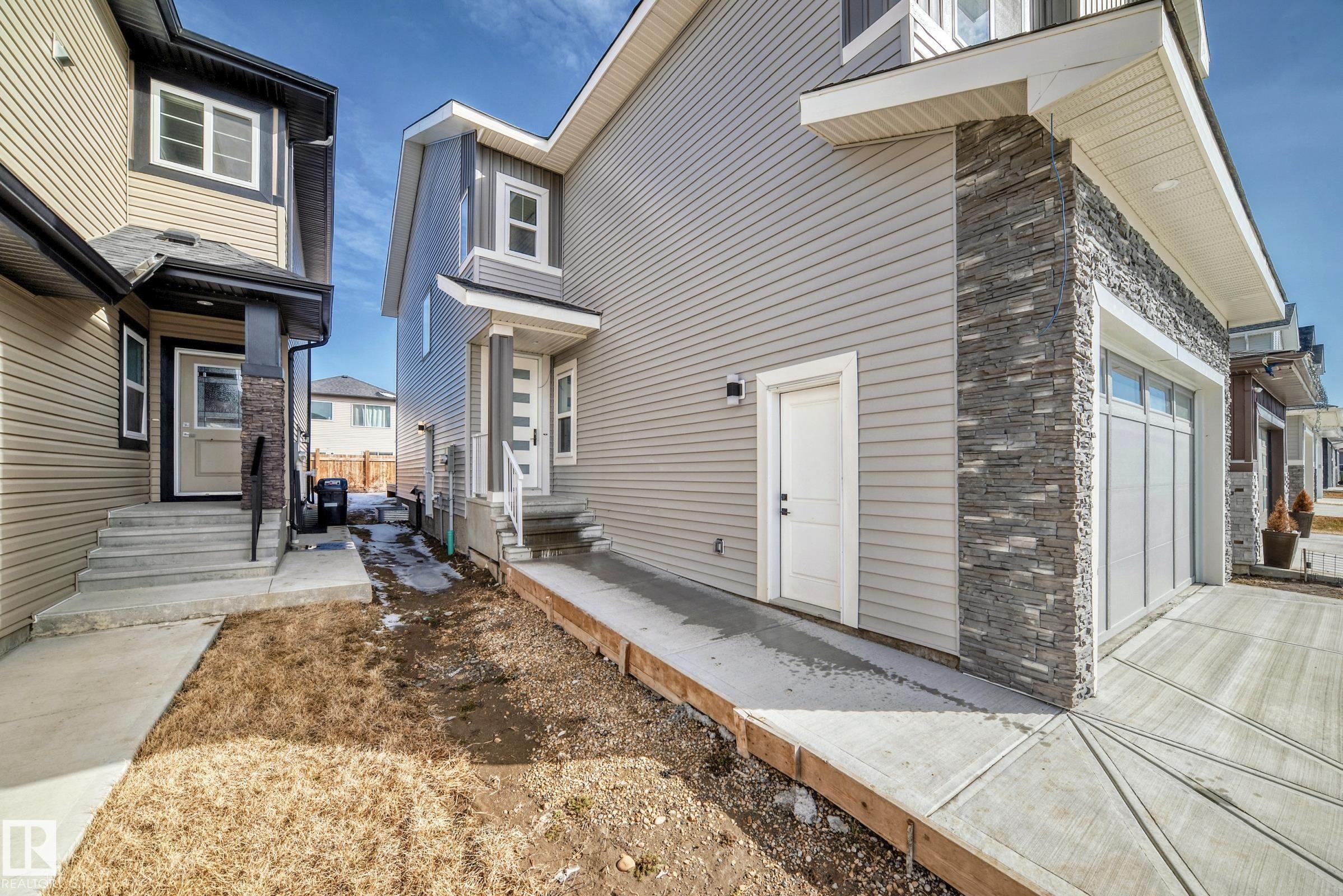 Contemporary exterior featuring light grey horizontal siding and stacked stone accents - 341 Roberts Wynd, Leduc, AB