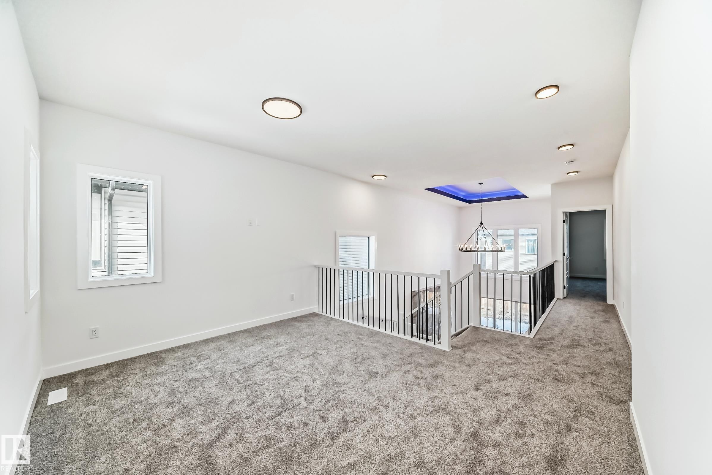 Carpeted upper-level landing featuring a metal spindle railing system, multiple windows, recessed lighting, and a chandelier with a blue-lit ceiling detail - 341 Roberts Wynd, Leduc, AB