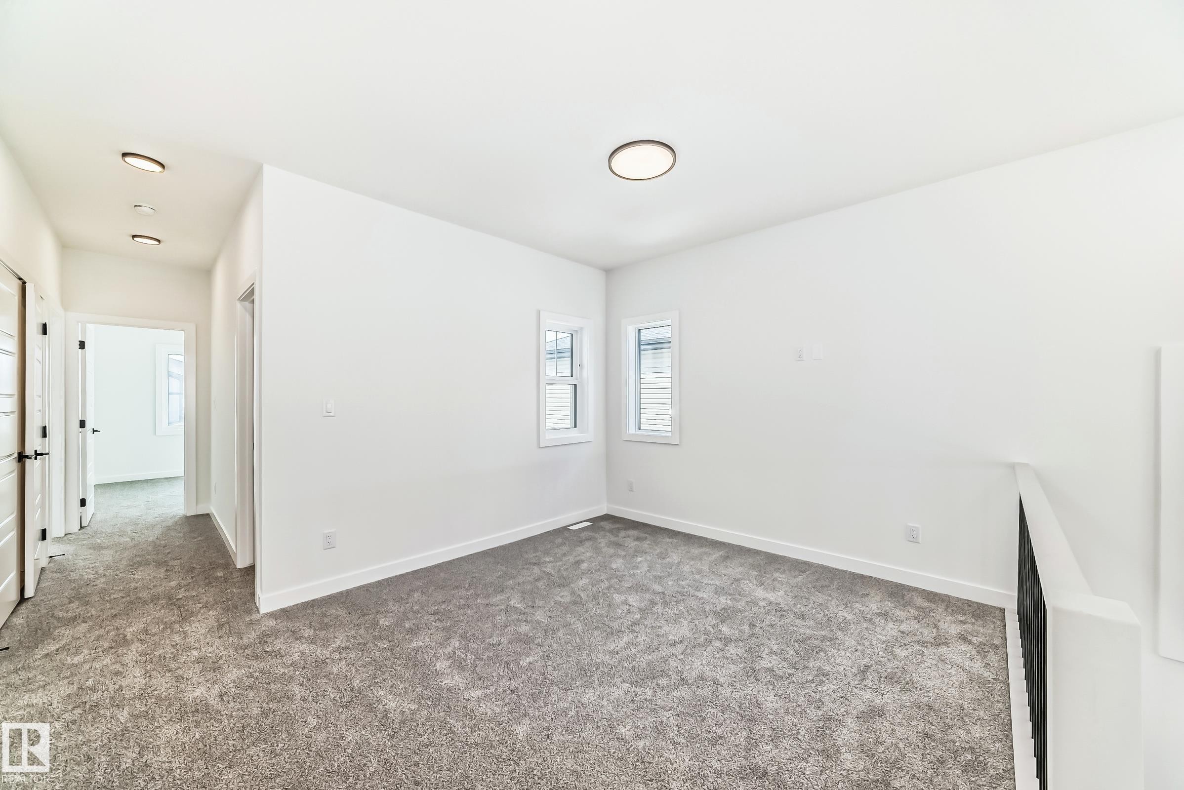 Neutral toned carpeted area featuring two windows with horizontal blinds, white baseboards, and a contemporary ceiling light fixture - 341 Roberts Wynd, Leduc, AB