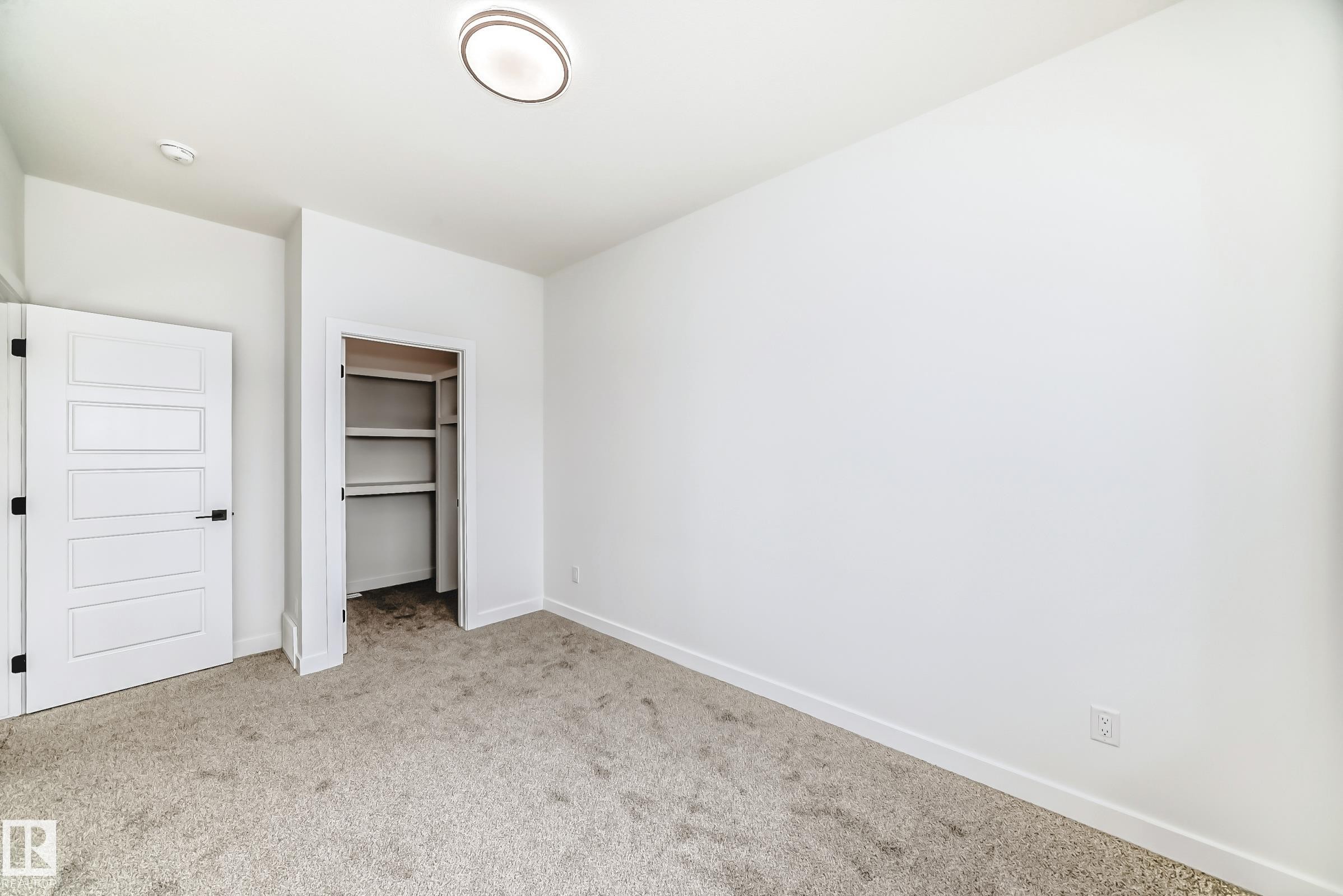 Neutral toned carpeting complementing white walls, a flush-mount ceiling light, a built-in closet with shelving and hanging rod, and a five-panel interior door with matte black hardware - 341 Roberts Wynd, Leduc, AB