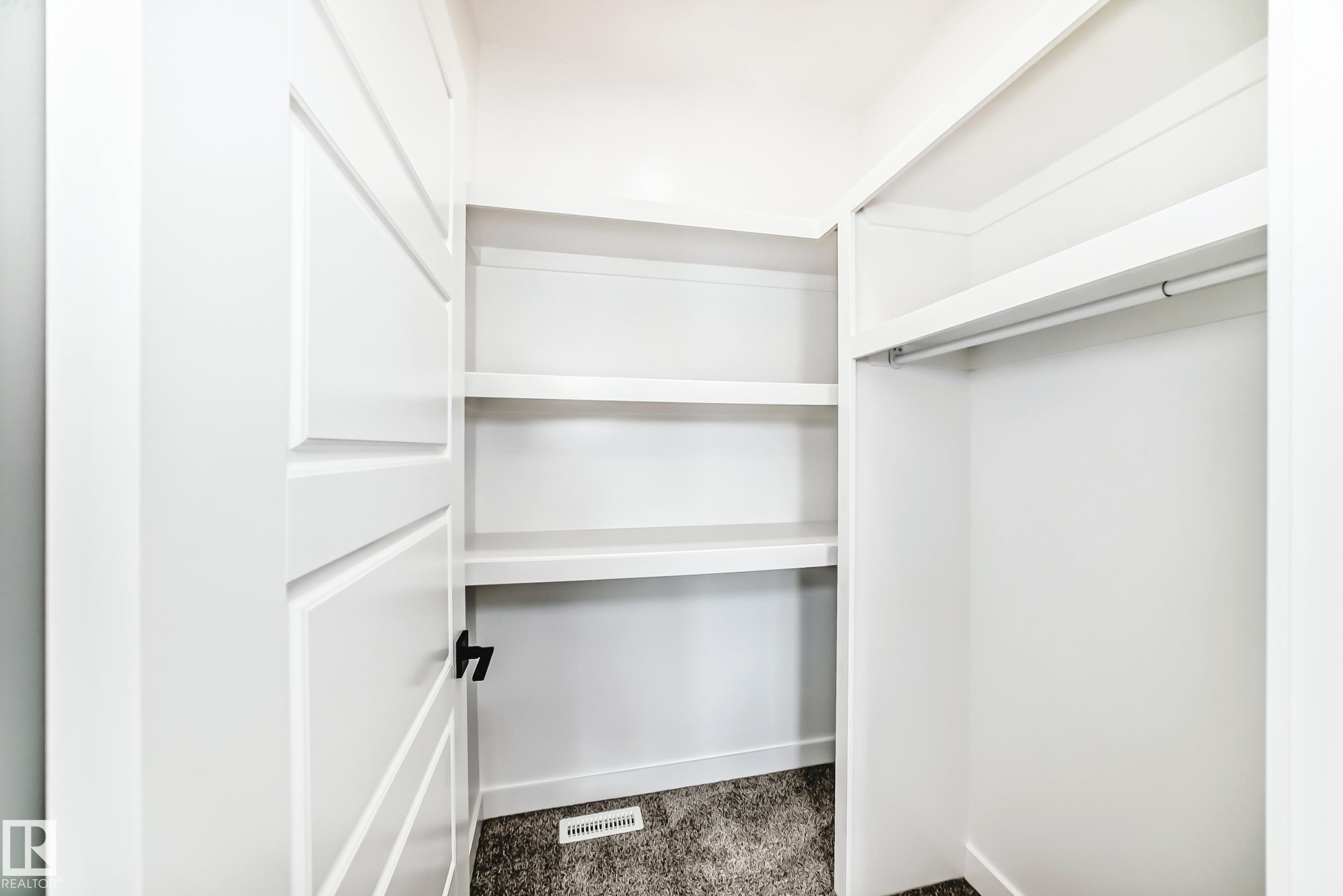 Recessed closet featuring white built-in shelving, a clothes rod, and dark carpet flooring - 341 Roberts Wynd, Leduc, AB