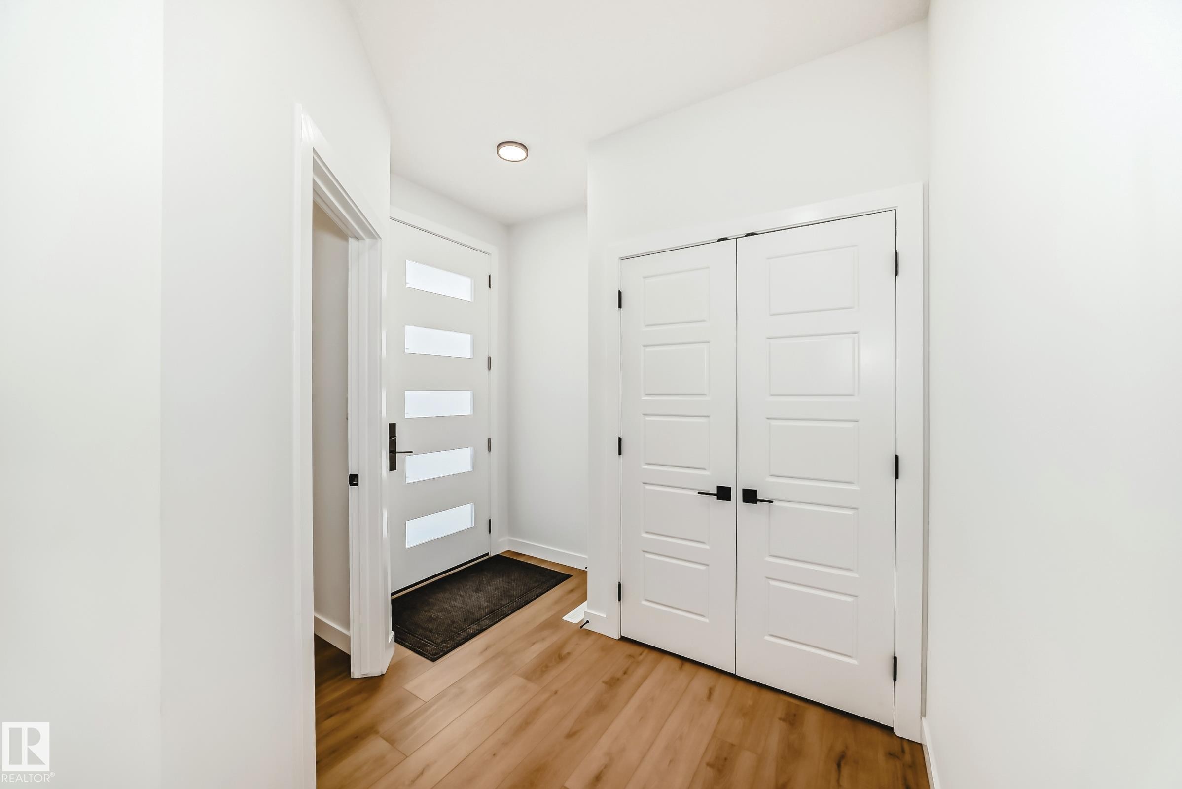 Entryway featuring a contemporary white door with frosted glass panels, wood-finish flooring, recessed lighting, and a double-door closet with black hardware - 341 Roberts Wynd, Leduc, AB