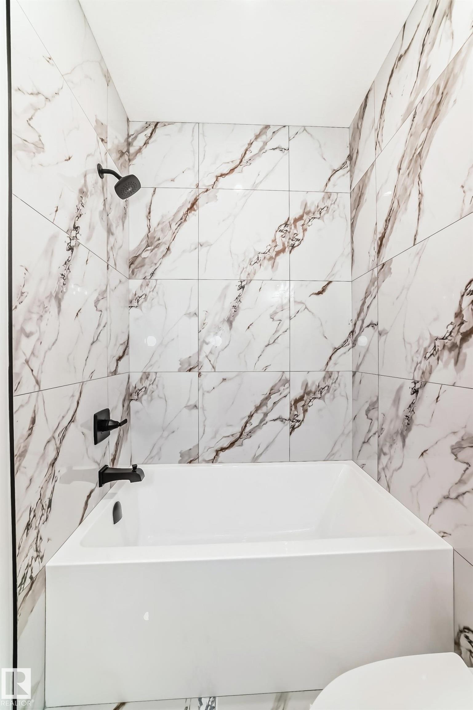 Bathroom featuring a white soaking tub with matte black fixtures, surrounded by large format porcelain wall tiles with a prominent veining pattern - 341 Roberts Wynd, Leduc, AB