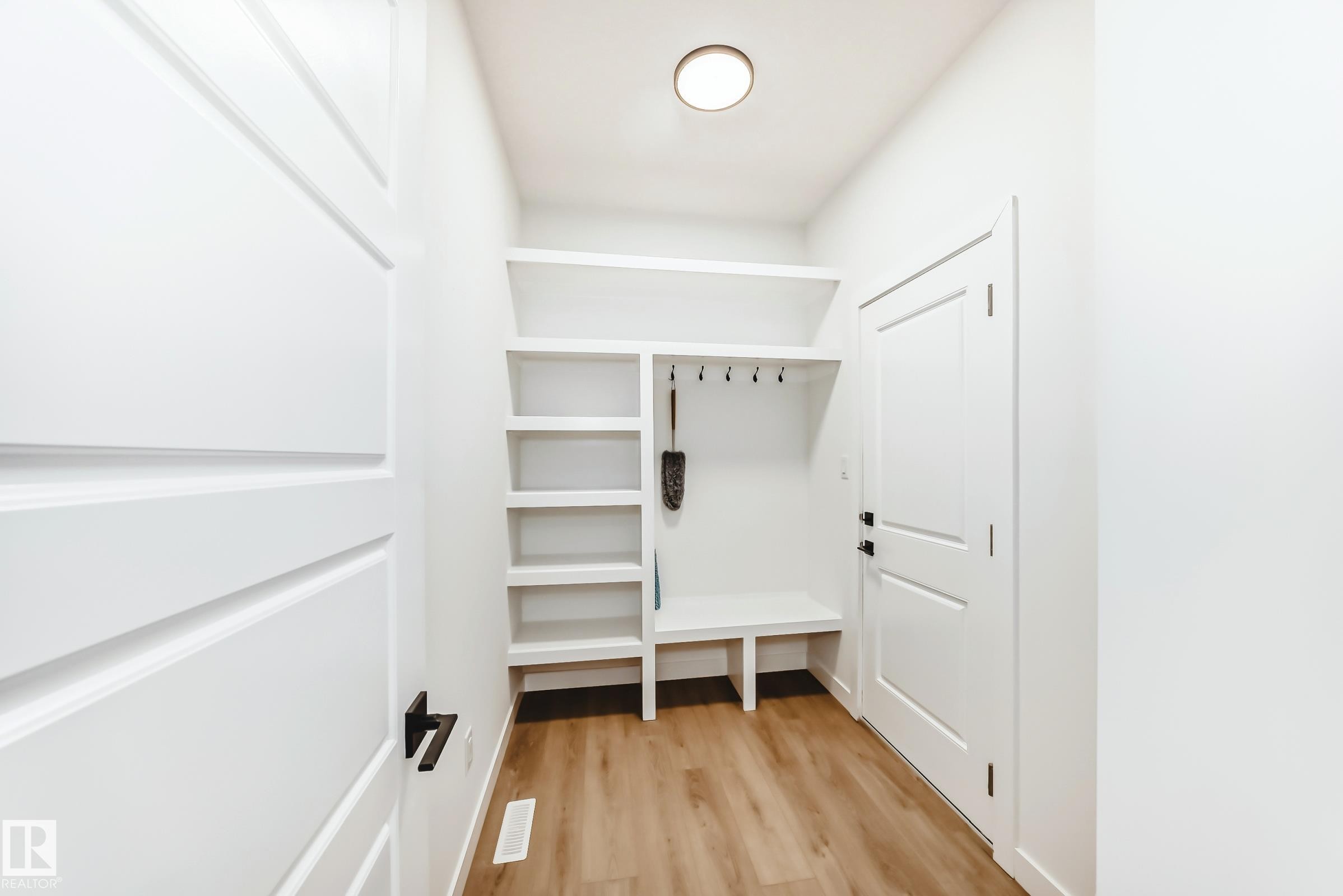 Entryway mudroom featuring integrated shelving, bench seating, coat hooks, and wood-finish flooring - 341 Roberts Wynd, Leduc, AB
