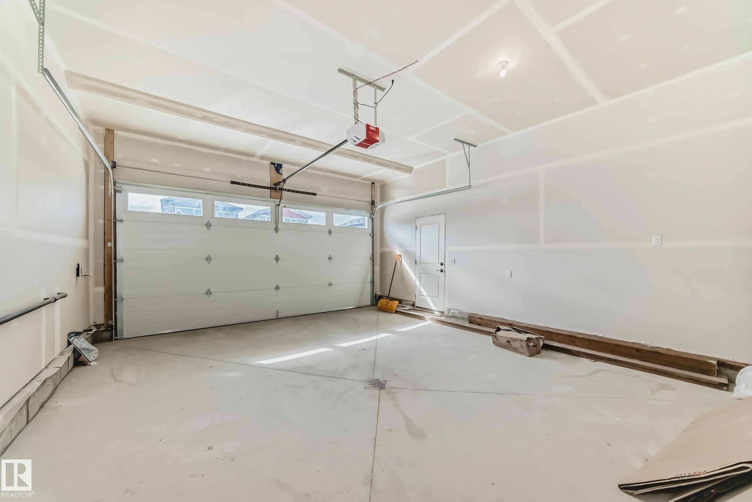Spacious garage featuring a concrete floor, an overhead garage door with upper window panels, and an interior access door - 341 Roberts Wynd, Leduc, AB