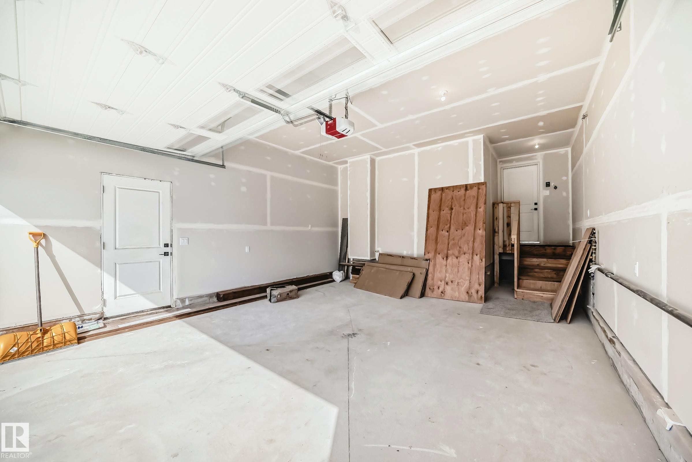 Spacious garage featuring unfinished drywall, a paneled overhead door, and a utility door - 341 Roberts Wynd, Leduc, AB