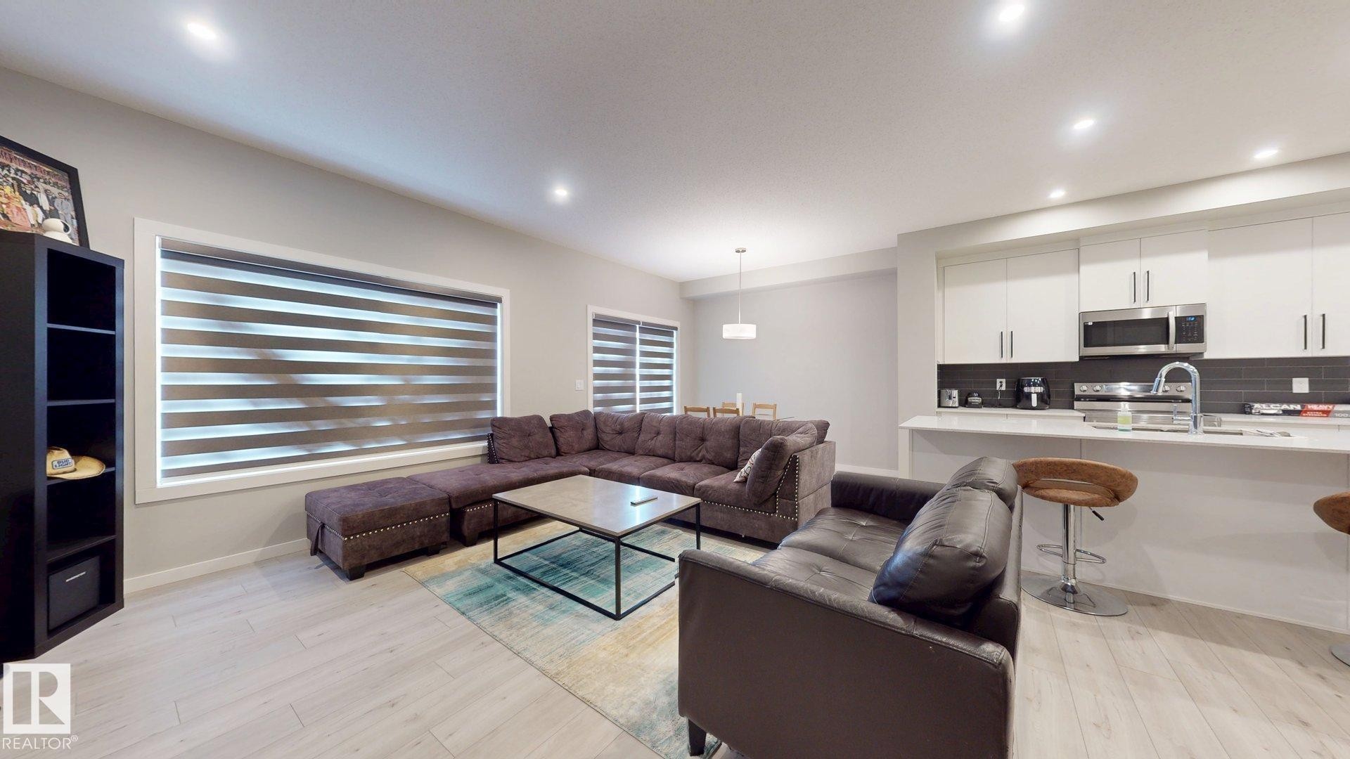 Open-concept living space with light wood-finish flooring, recessed lighting, and expansive windows featuring horizontal blinds - 607 31 Avenue, Edmonton, AB