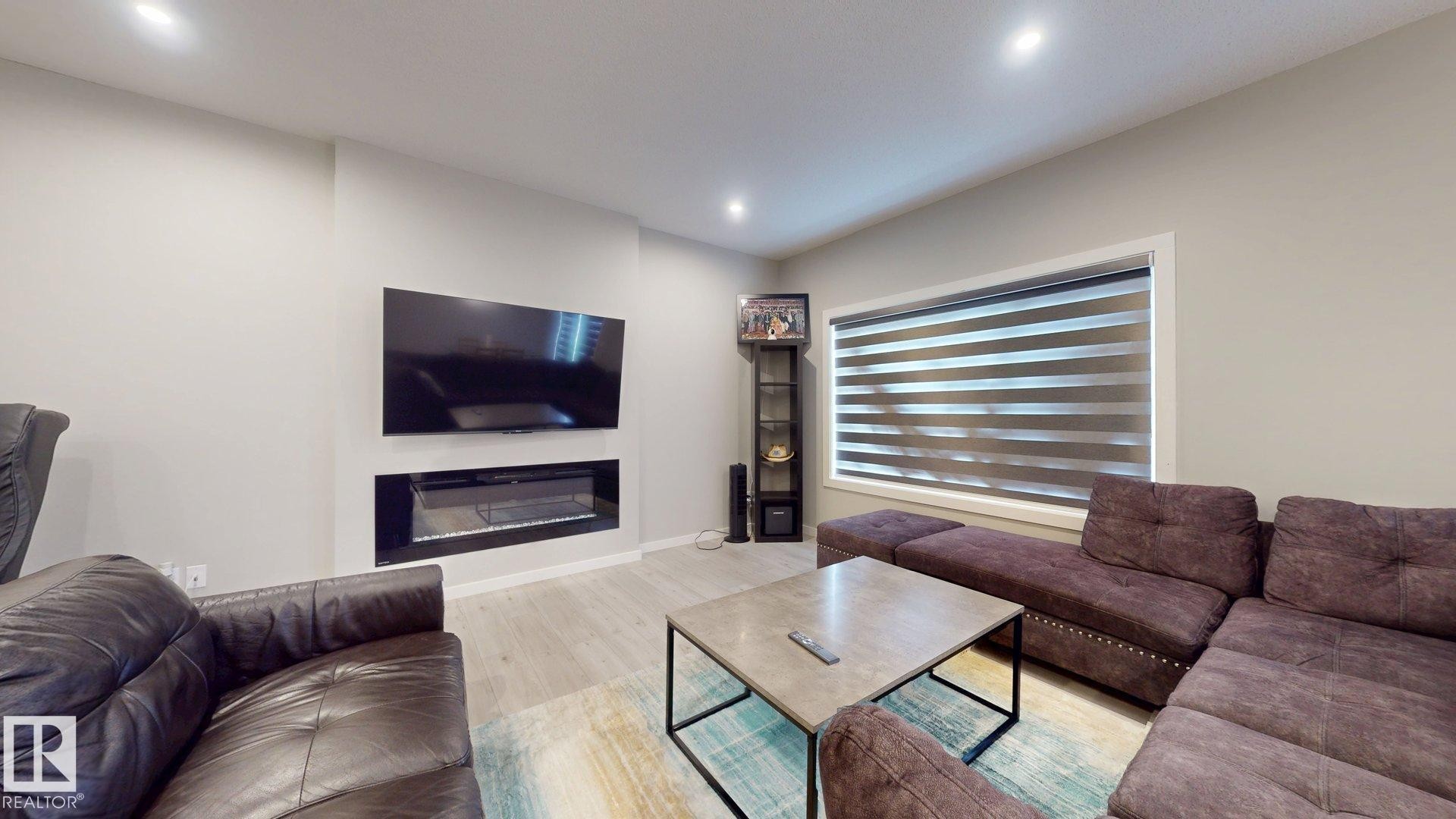 Living area featuring a mounted entertainment display, an integrated linear fireplace, and wood-finish flooring - 607 31 Avenue, Edmonton, AB