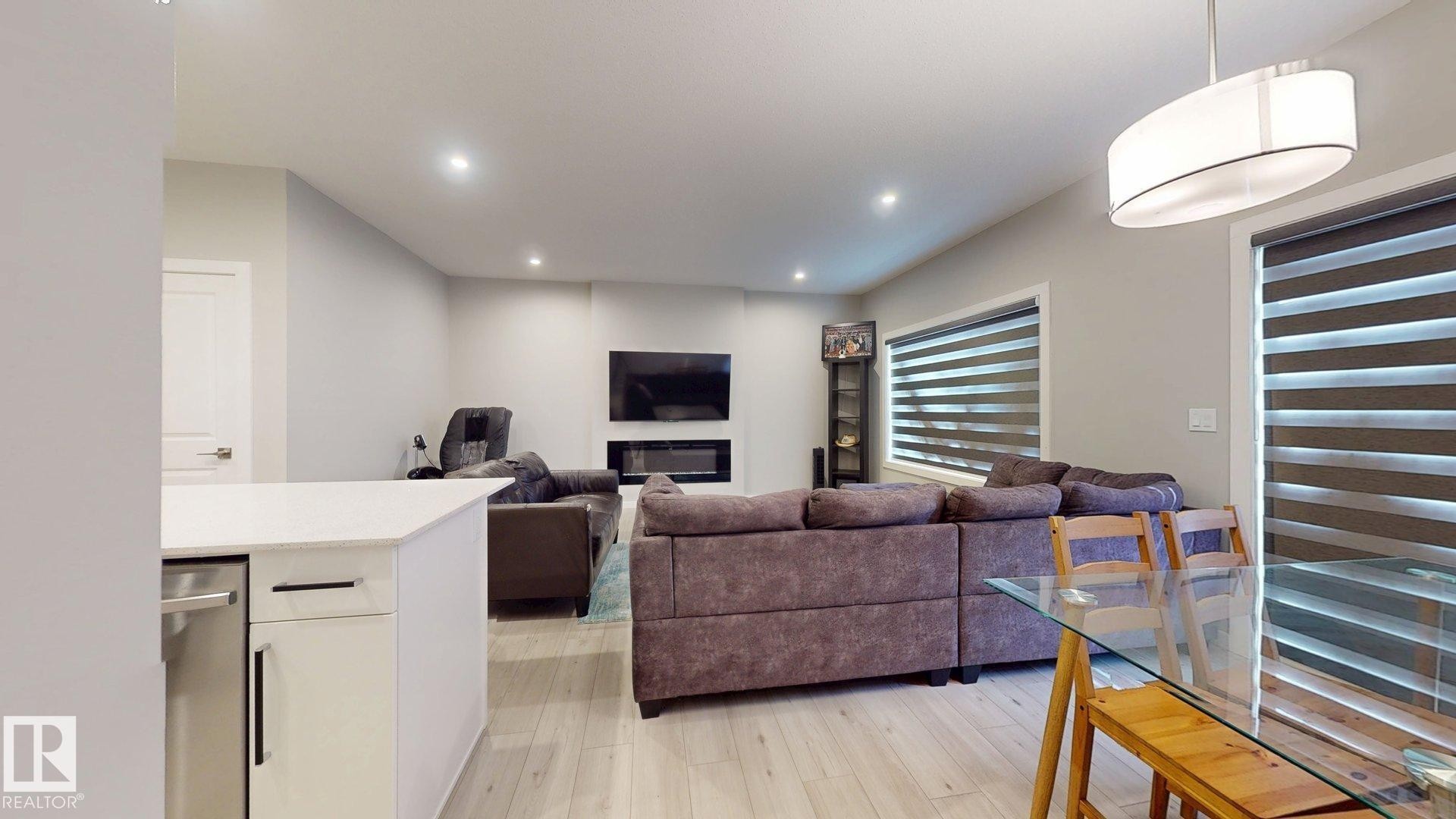 Open-concept living area featuring light wood-finish flooring, recessed lighting, and a contemporary fireplace with a built-in television mount - 607 31 Avenue, Edmonton, AB