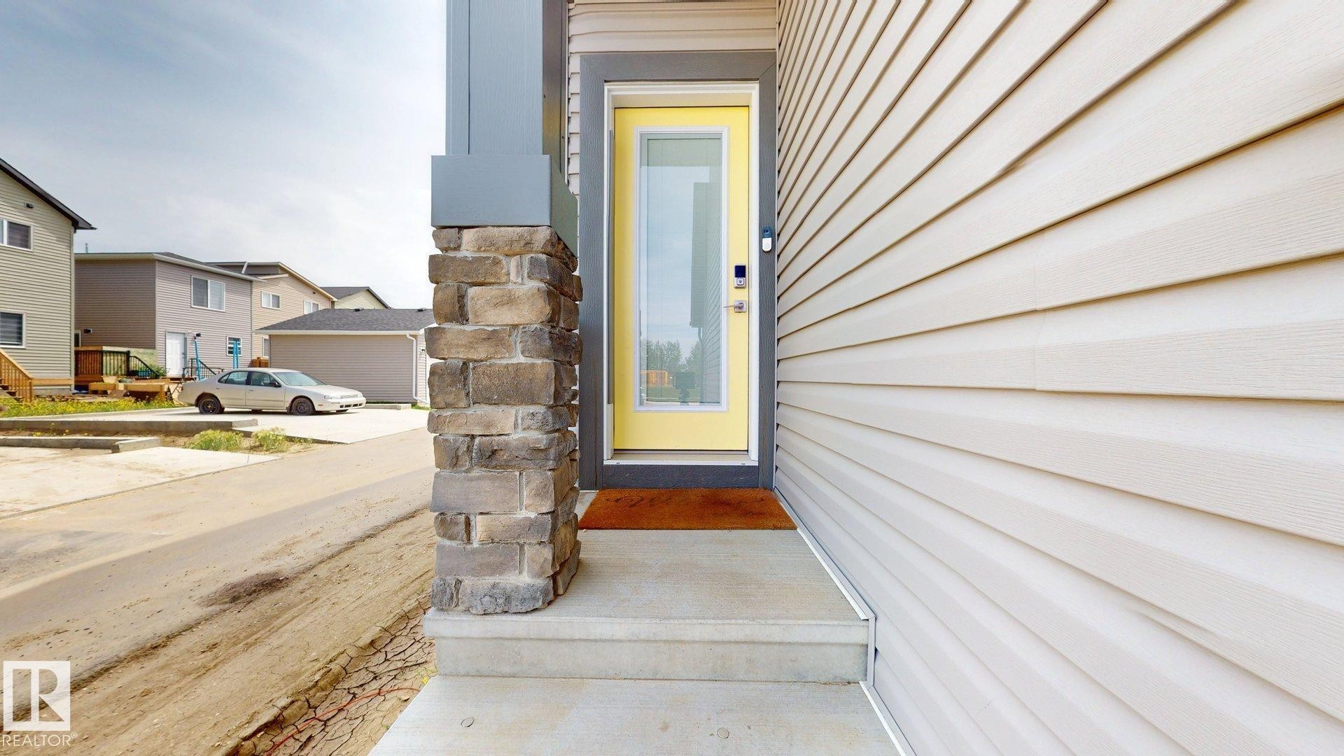Inviting front entrance featuring a bright yellow door with glass insert, concrete steps, and a stone-clad pillar accent - 607 31 Avenue, Edmonton, AB