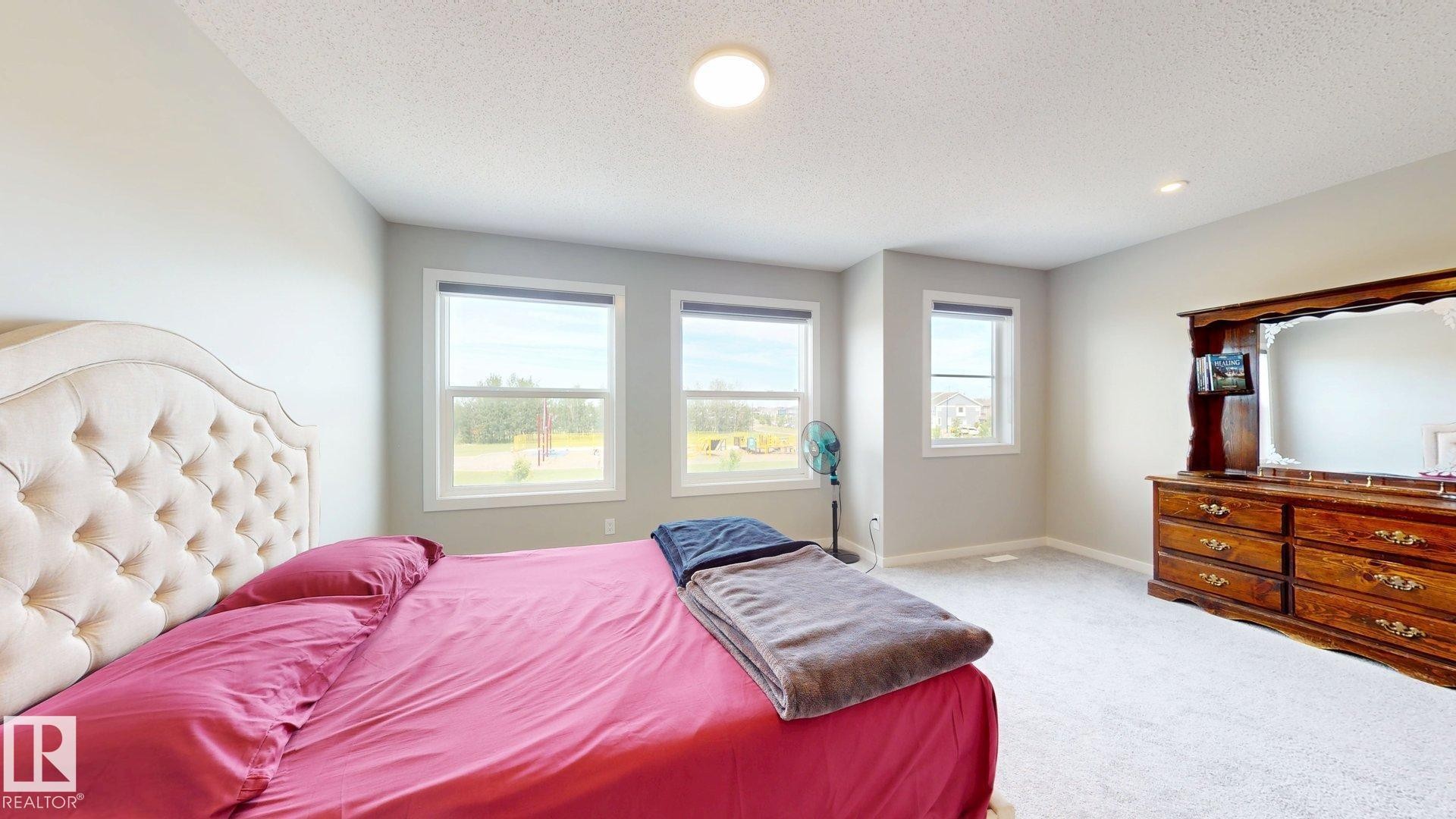 Neutral-toned bedroom featuring three windows, recessed lighting, and soft gray carpeting - 607 31 Avenue, Edmonton, AB