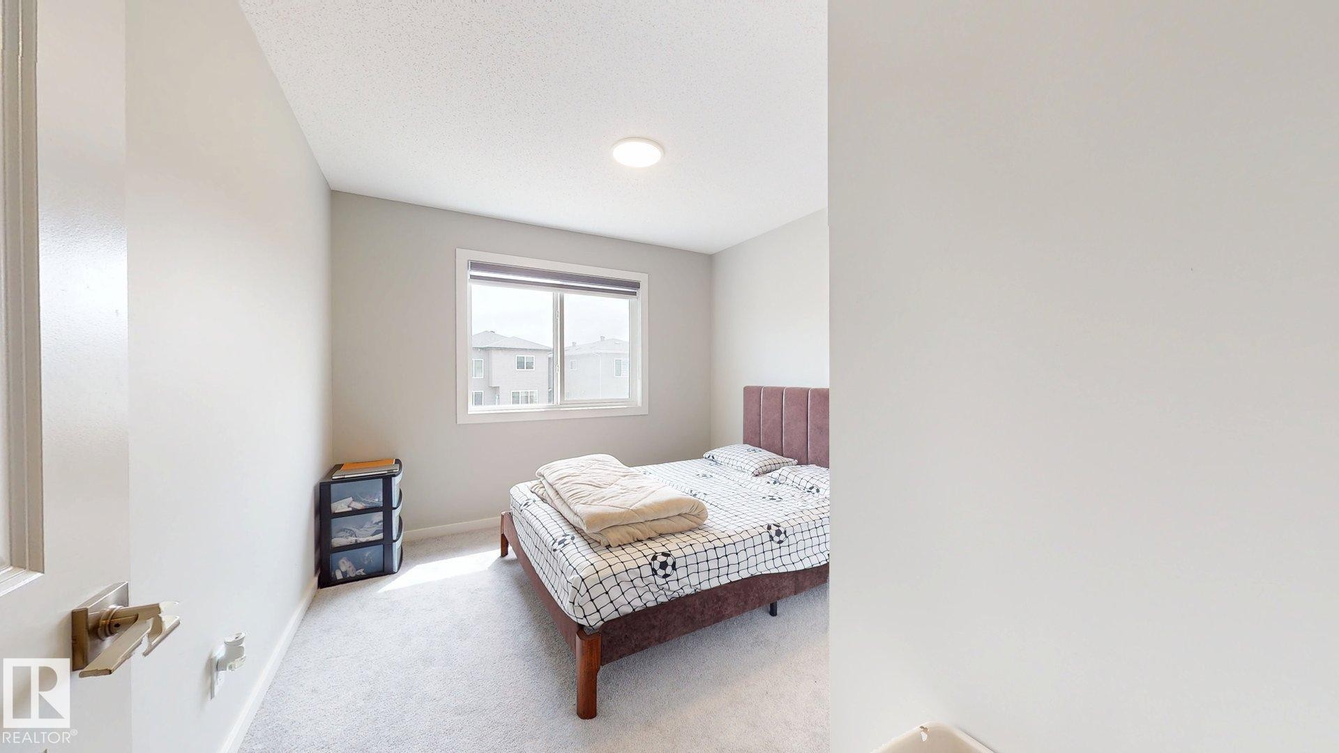 Bedroom featuring a light gray carpeted floor, light gray wall paint, and a rectangular window with a white frame - 607 31 Avenue, Edmonton, AB