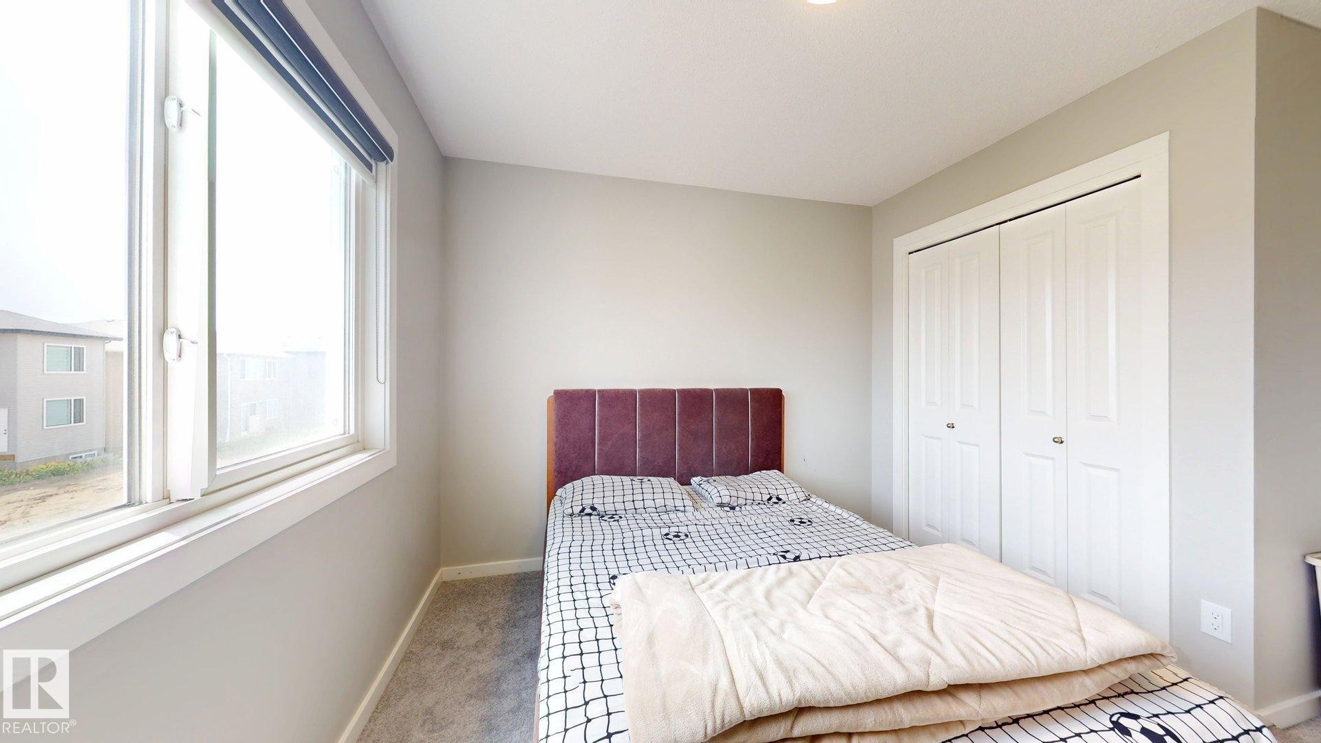 Light-filled room featuring a large window with roller shades, neutral gray walls, and plush gray carpeting - 607 31 Avenue, Edmonton, AB