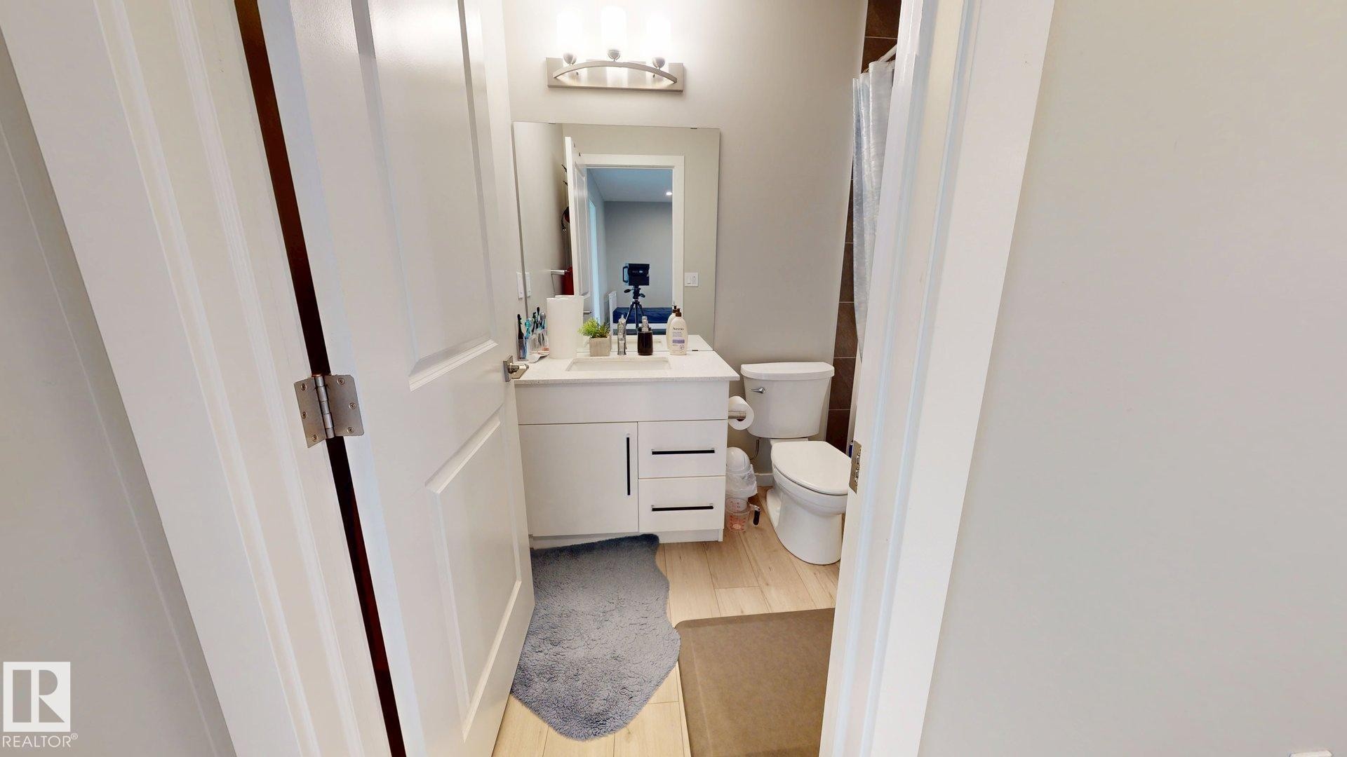 Bathroom featuring a white vanity with integrated sink, chrome faucet, wall-mounted mirror, and overhead light fixture - 607 31 Avenue, Edmonton, AB