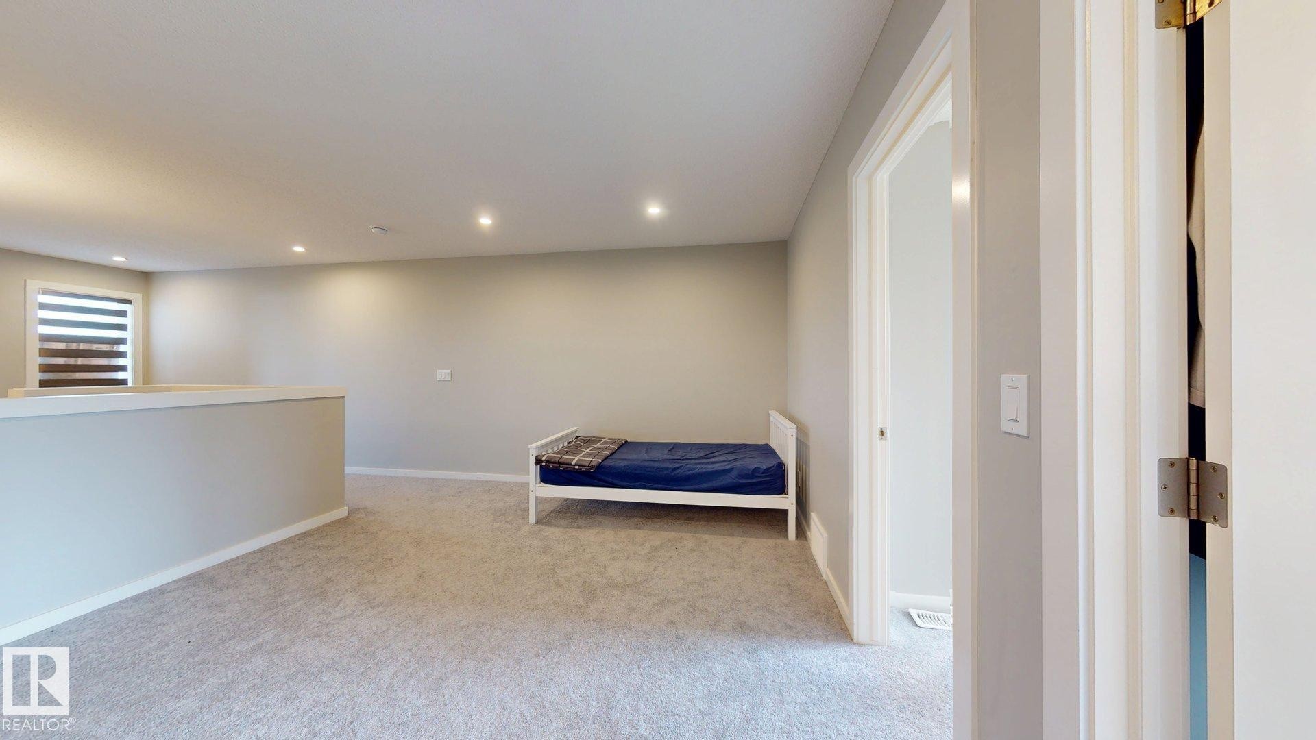 Spacious carpeted room featuring recessed lighting, a half-wall partition, and a window with horizontal blinds - 607 31 Avenue, Edmonton, AB