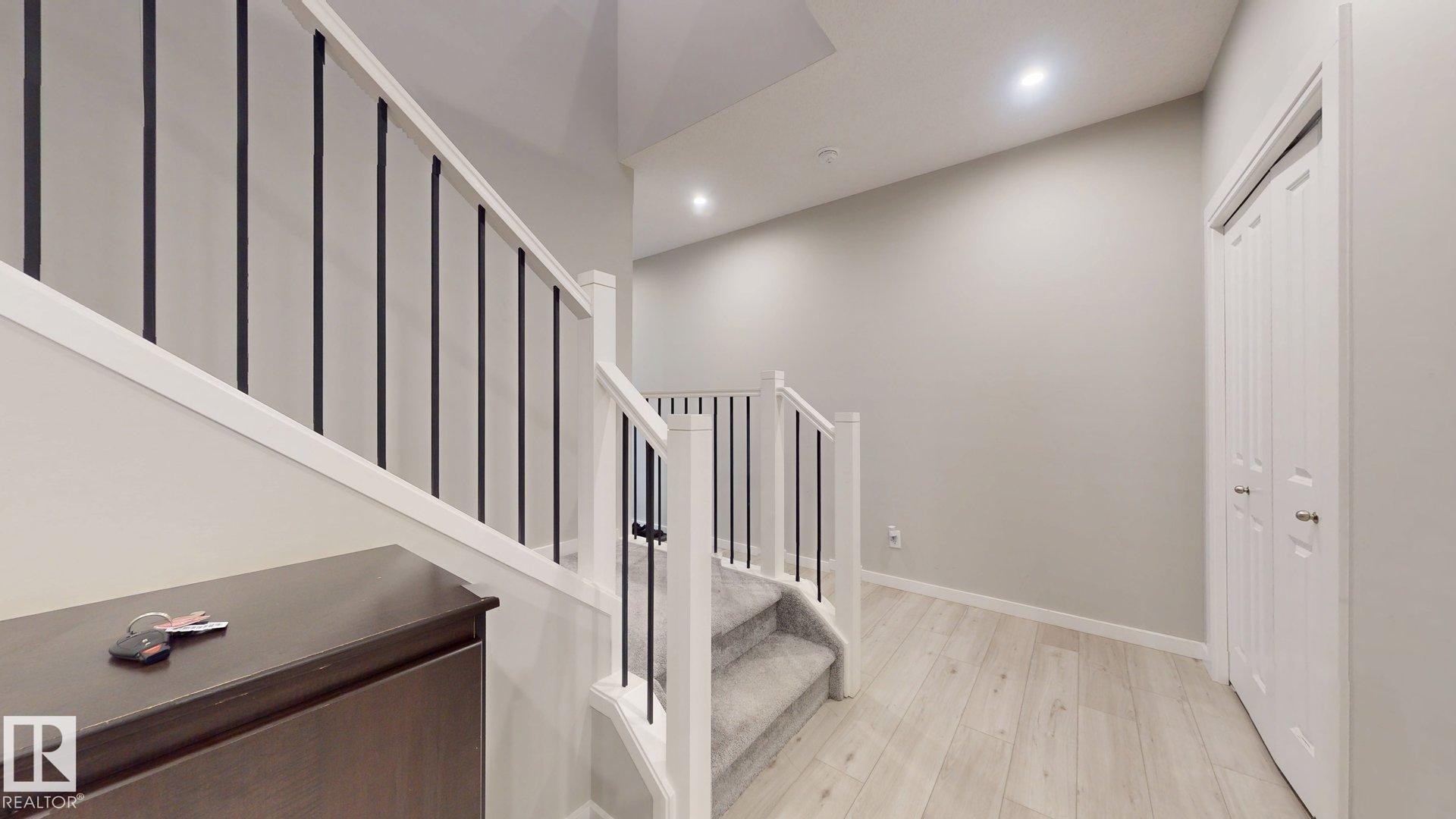Staircase with white newel posts and black metal balusters, featuring light wood-finish flooring, recessed lighting, and white bi-fold doors - 607 31 Avenue, Edmonton, AB