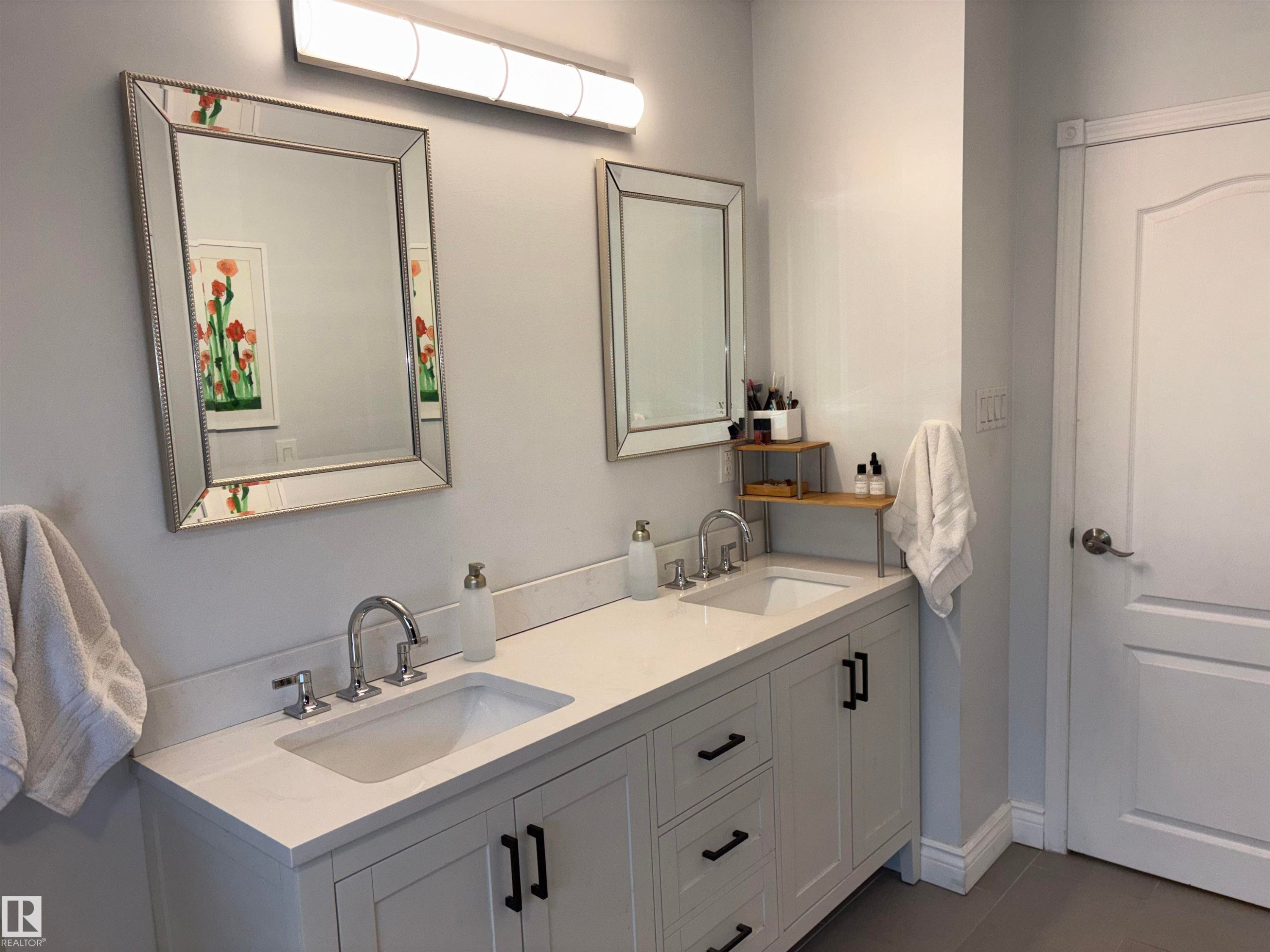 Bathroom featuring a double vanity with light-colored countertops, dual undermount sinks, chrome fixtures, and white shaker-style cabinetry with black pulls - 14016 85 Avenue Nw, Edmonton, AB - Indoor Photo Showing Bathroom
