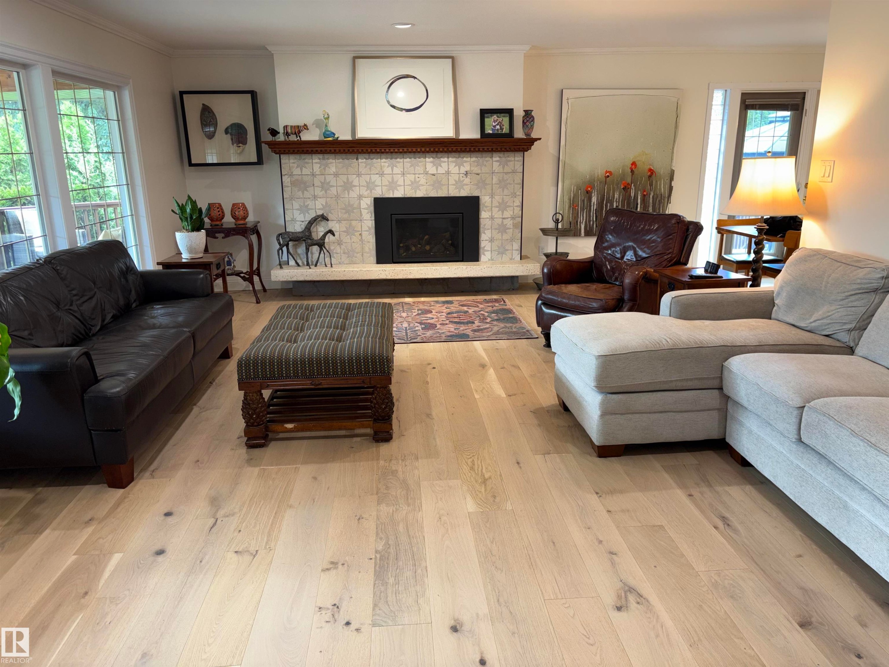 Spacious living area featuring light wood-finish flooring, a tiled fireplace with a wood mantel, crown molding, and large windows with leaded glass accents - 14016 85 Avenue Nw, Edmonton, AB - Indoor Photo Showing Living Room With Fireplace