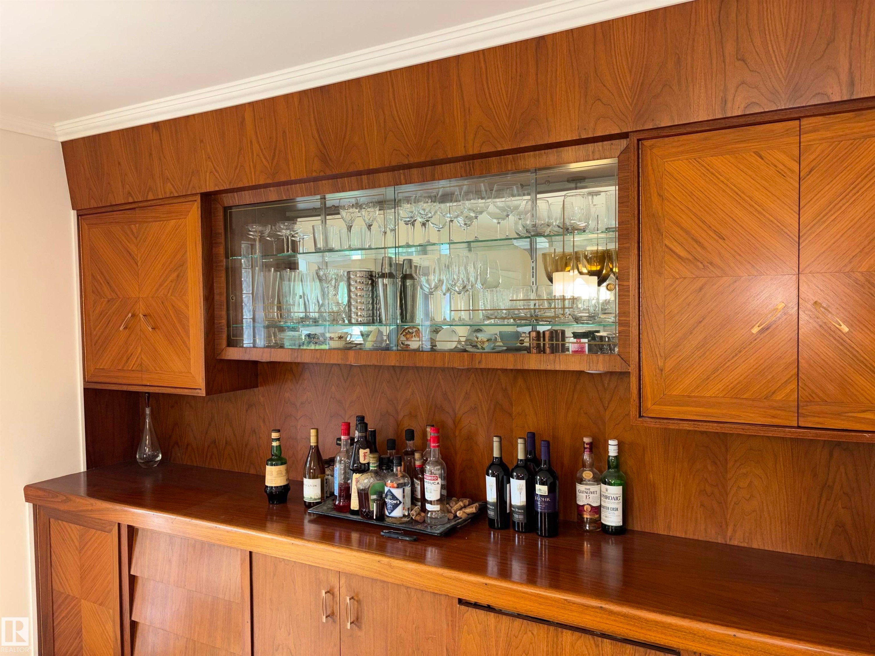 Custom built-in cabinetry featuring wood-finish construction with a patterned inlay, glass-front display shelving, an integrated counter surface, and matching base storage - 14016 85 Avenue Nw, Edmonton, AB - Indoor Photo Showing Other Room