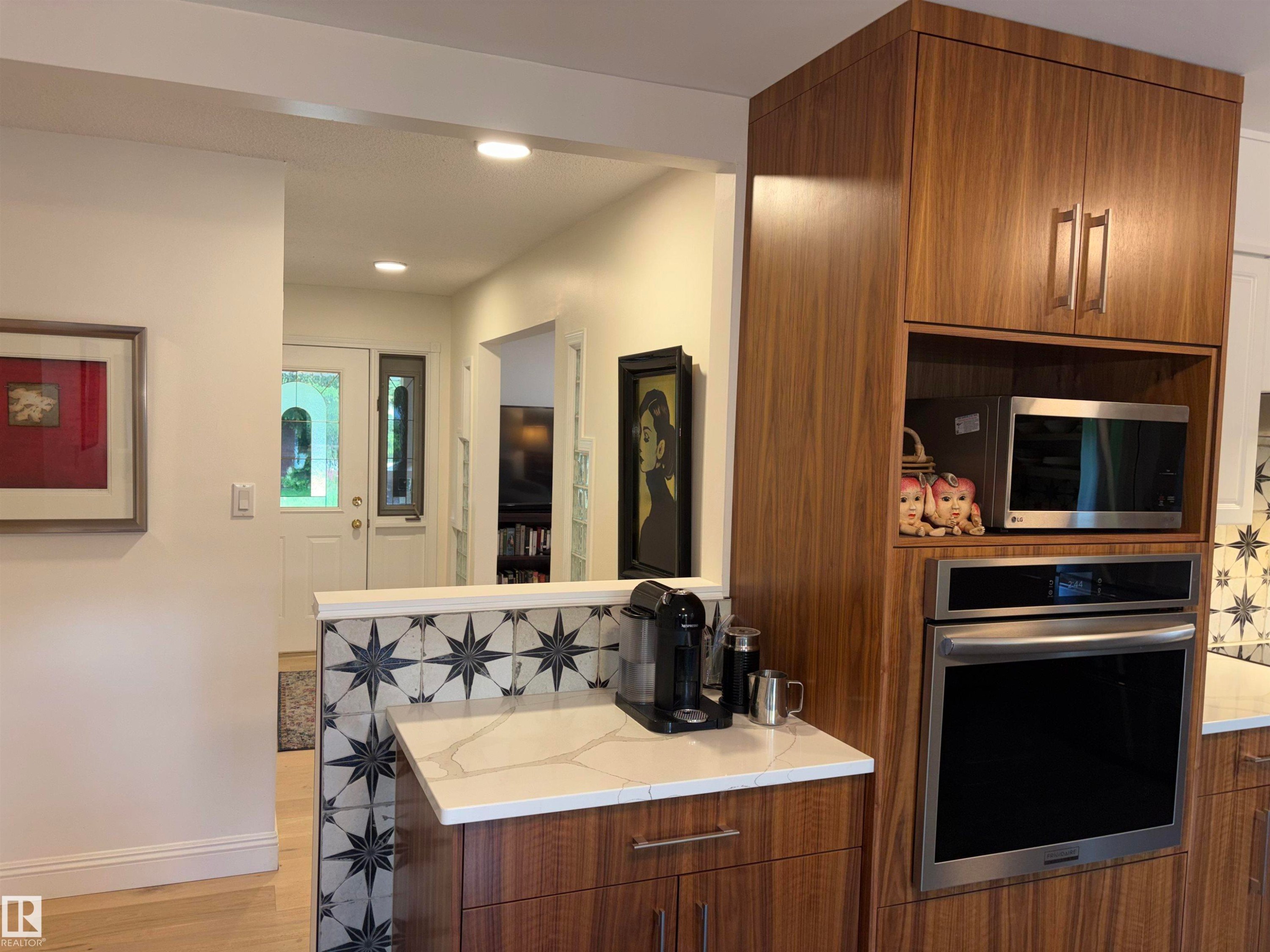 Kitchen featuring integrated wood-finish cabinetry, built-in stainless steel microwave and oven, a patterned tile accent wall, and solid surface countertops - 14016 85 Avenue Nw, Edmonton, AB - Indoor Photo Showing Kitchen