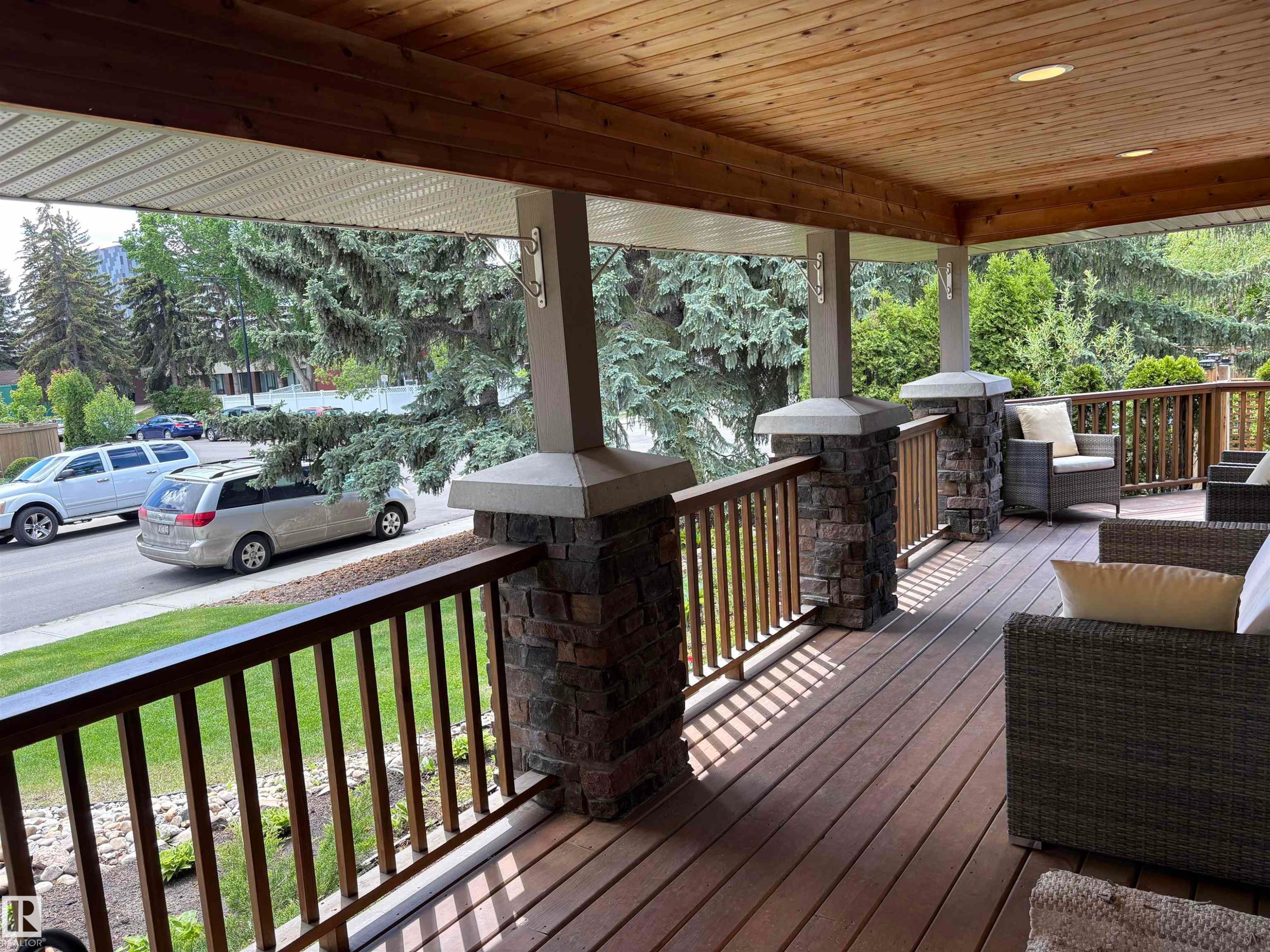 Spacious covered porch featuring a wood-finish plank deck, stone-accented columns, wood-paneled ceiling, and recessed lighting - 14016 85 Avenue Nw, Edmonton, AB - Outdoor With Deck Patio Veranda With Exterior