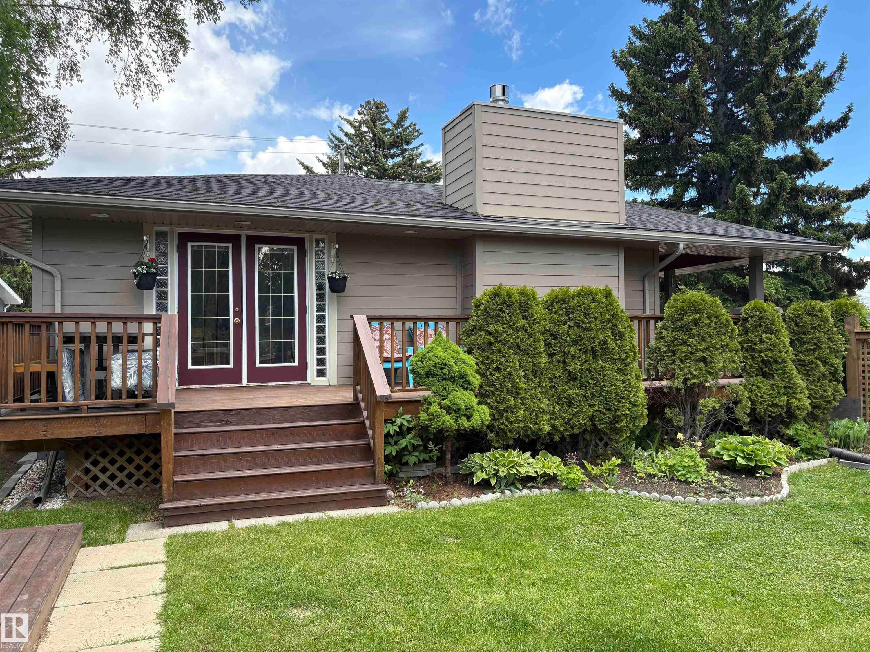 Rear exterior featuring a spacious wooden deck with direct access via double glass-paneled doors, a manicured lawn, and mature evergreen shrubs - 14016 85 Avenue Nw, Edmonton, AB - Outdoor With Deck Patio Veranda