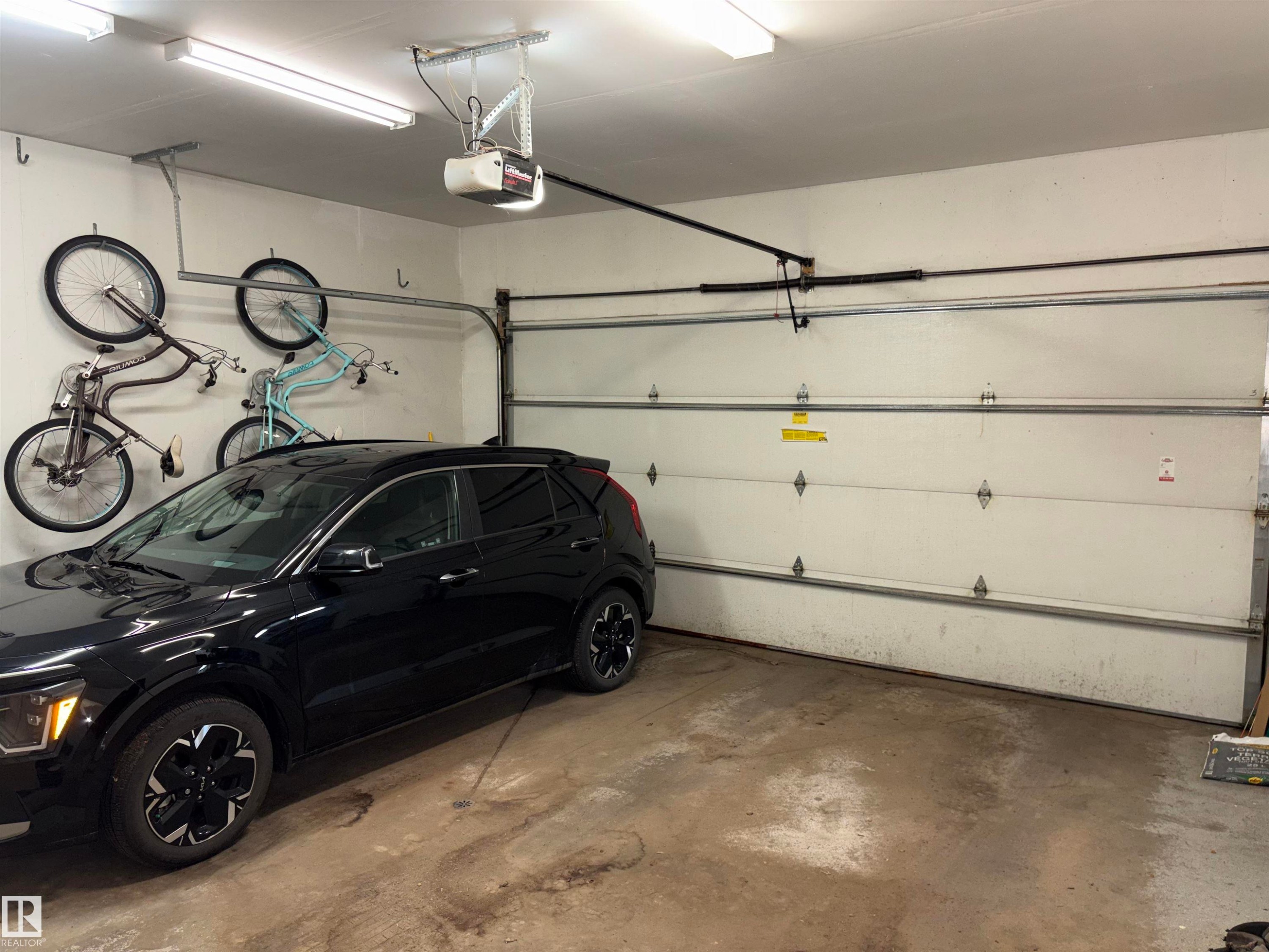 Attached garage featuring a sectional overhead door, concrete flooring, overhead lighting, and an automatic garage door opener - 14016 85 Avenue Nw, Edmonton, AB - Indoor Photo Showing Garage
