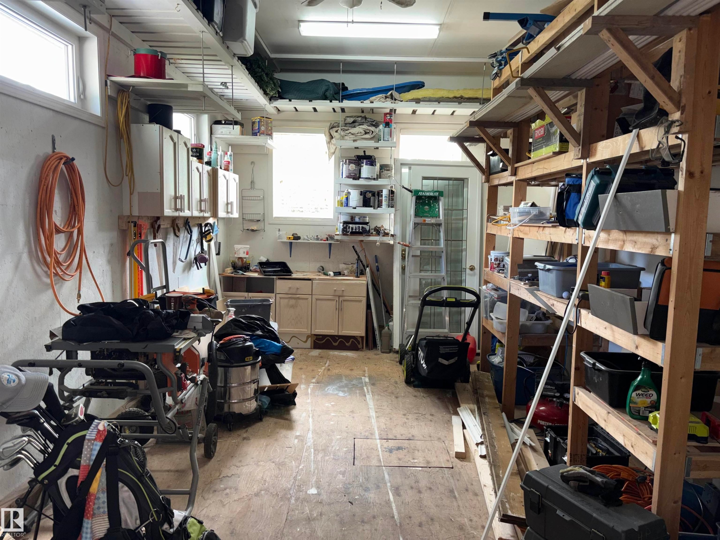 Spacious utility area featuring multiple windows, built-in overhead storage shelves, base cabinetry with countertops, and a service door - 14016 85 Avenue Nw, Edmonton, AB - Indoor Photo Showing Garage