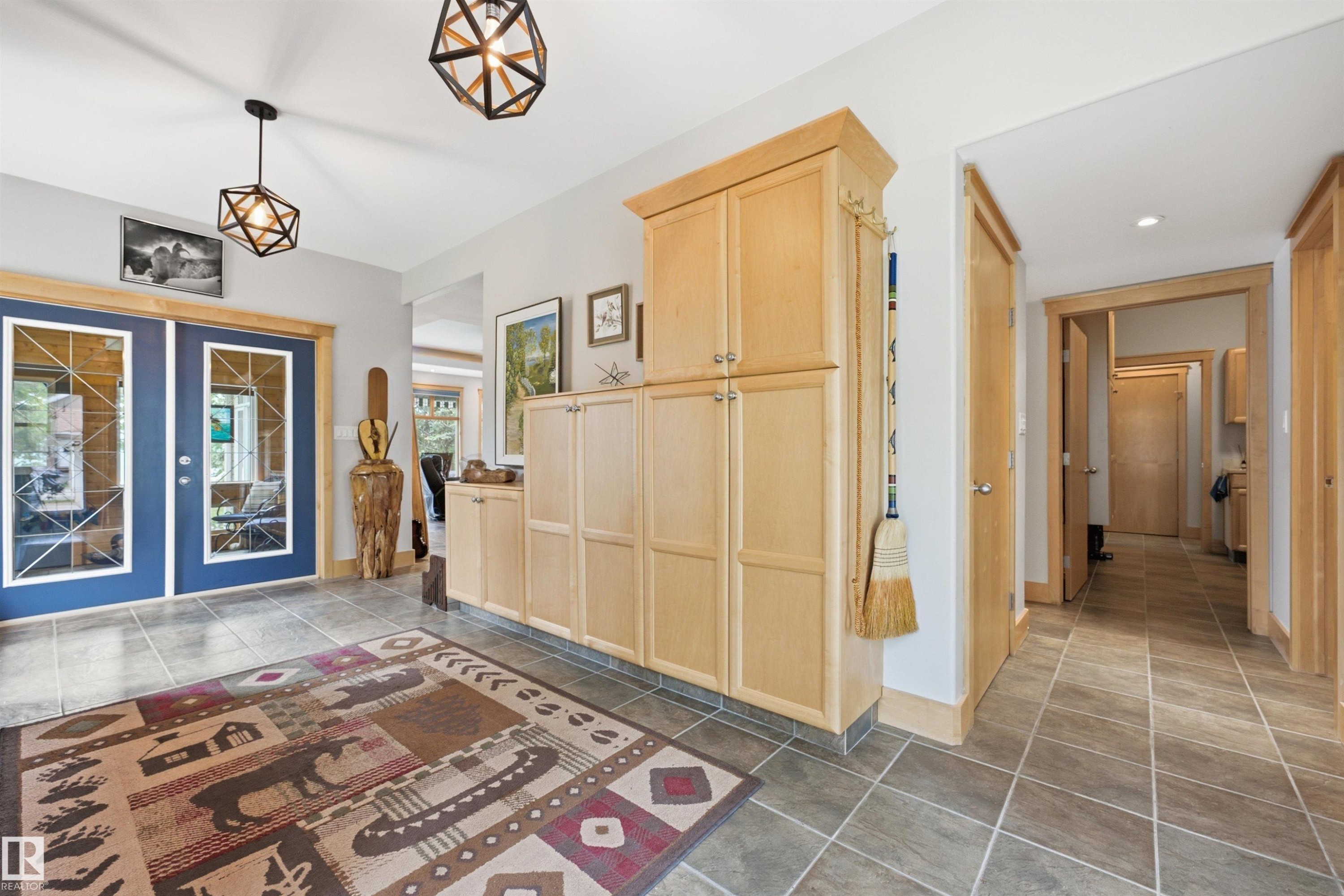 Entryway featuring dual blue doors with glass panes, geometric pendant lighting, built-in natural wood cabinetry, and neutral tile flooring - A38 Bernice Ave, Rural Leduc County, AB