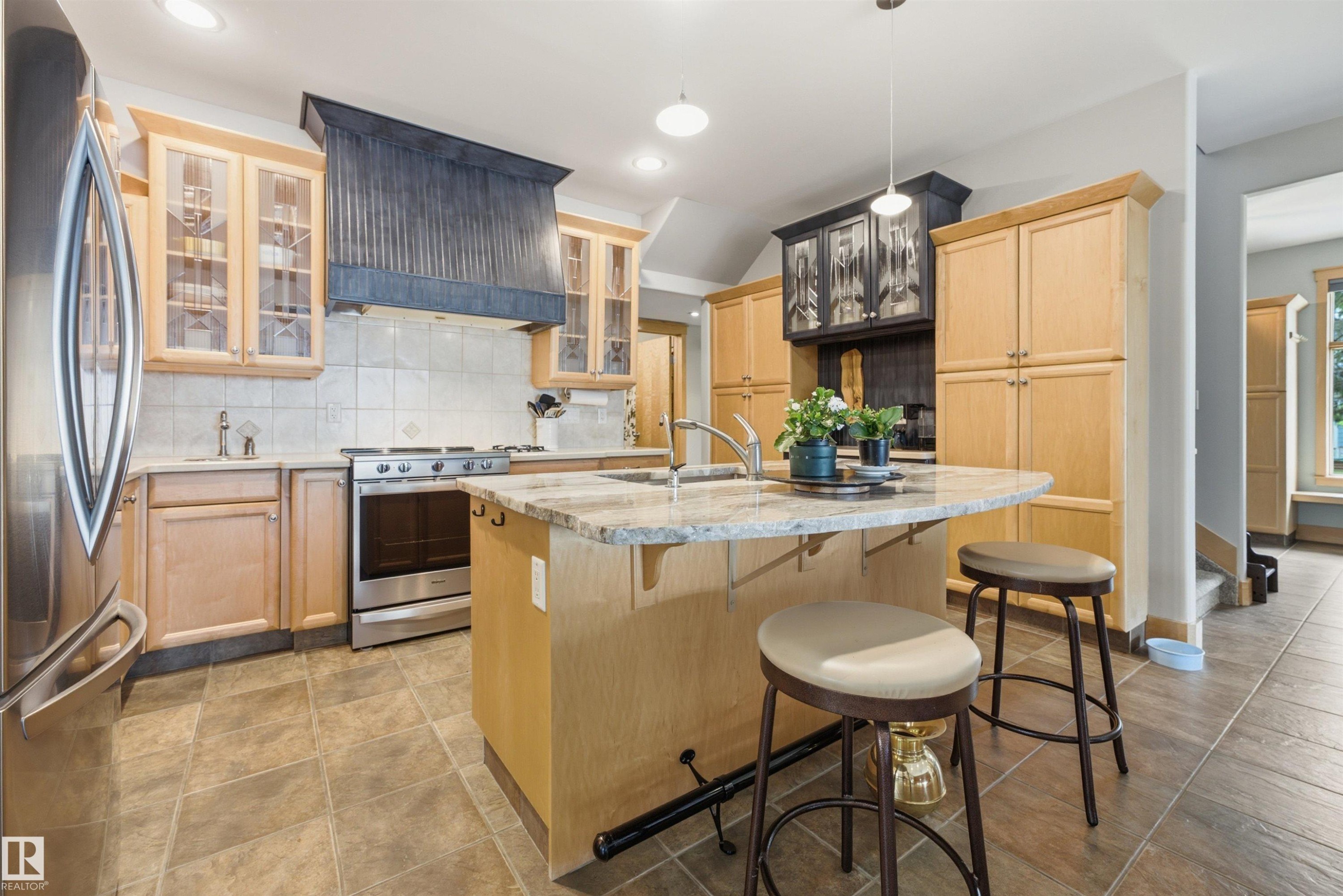 Kitchen featuring an island with a breakfast bar, granite countertops, stainless steel appliances, light wood cabinetry, and tiled flooring - A38 Bernice Ave, Rural Leduc County, AB