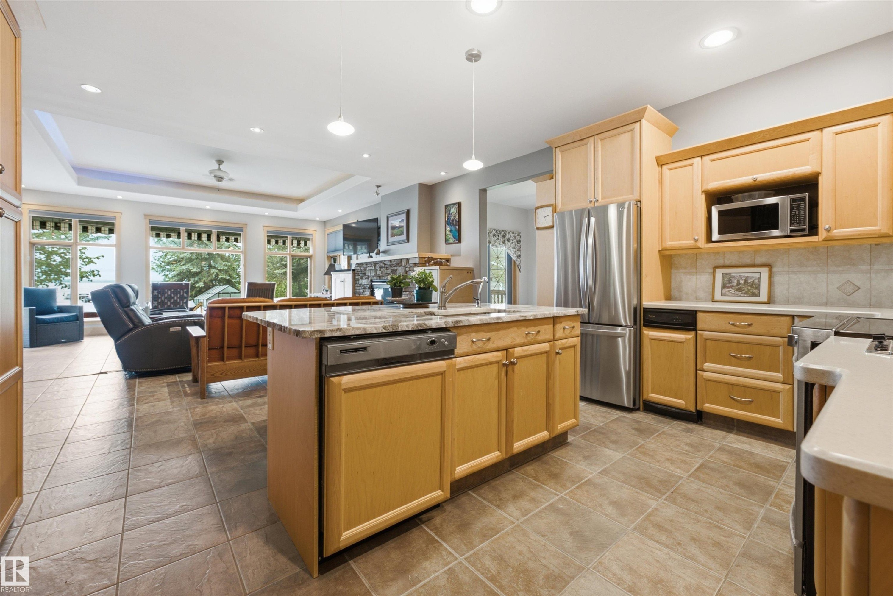 Kitchen featuring light-toned wood cabinetry and a central island with a stone-finish countertop - A38 Bernice Ave, Rural Leduc County, AB