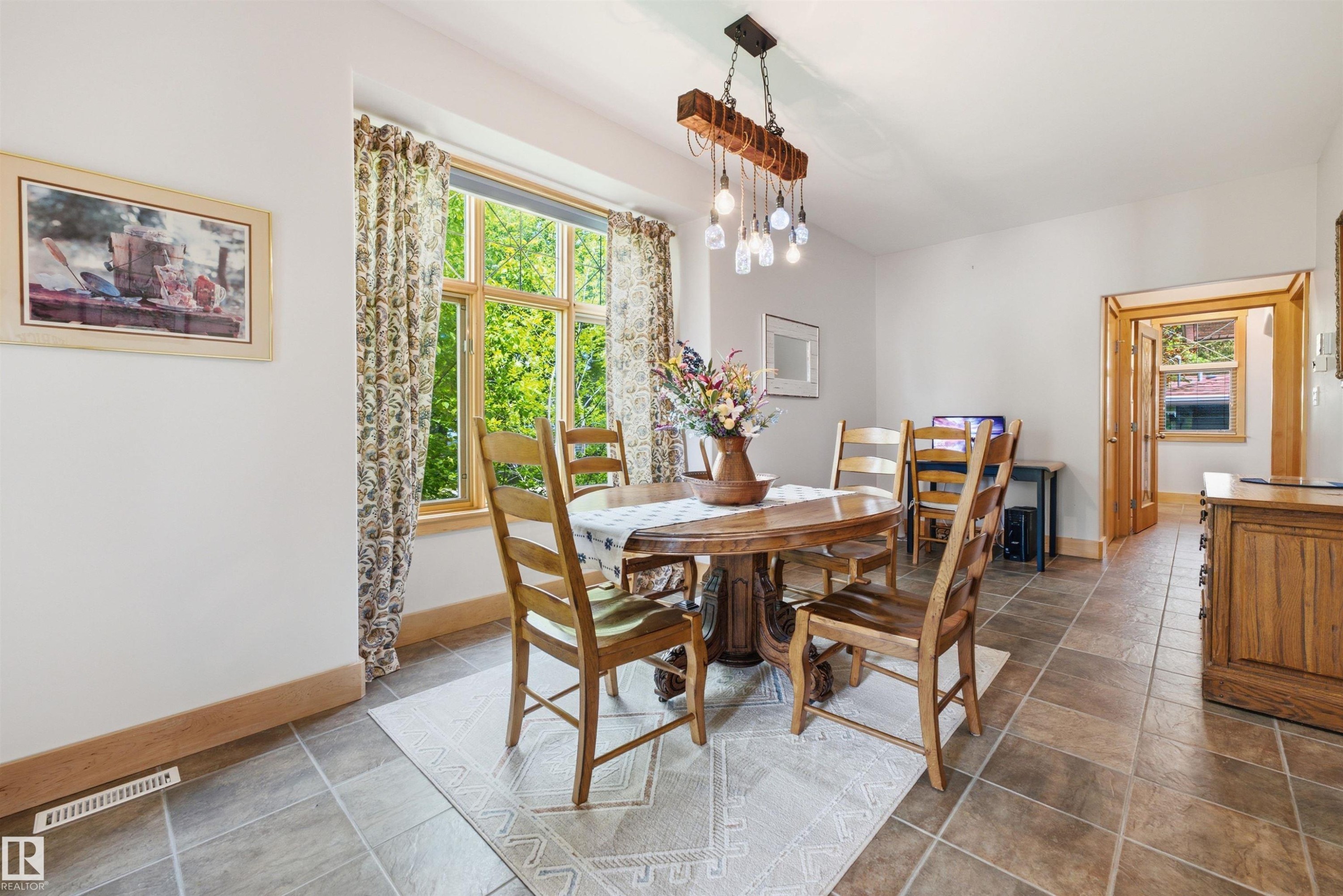 Dining area featuring a large window with wood trim, tile flooring, and a decorative light fixture - A38 Bernice Ave, Rural Leduc County, AB