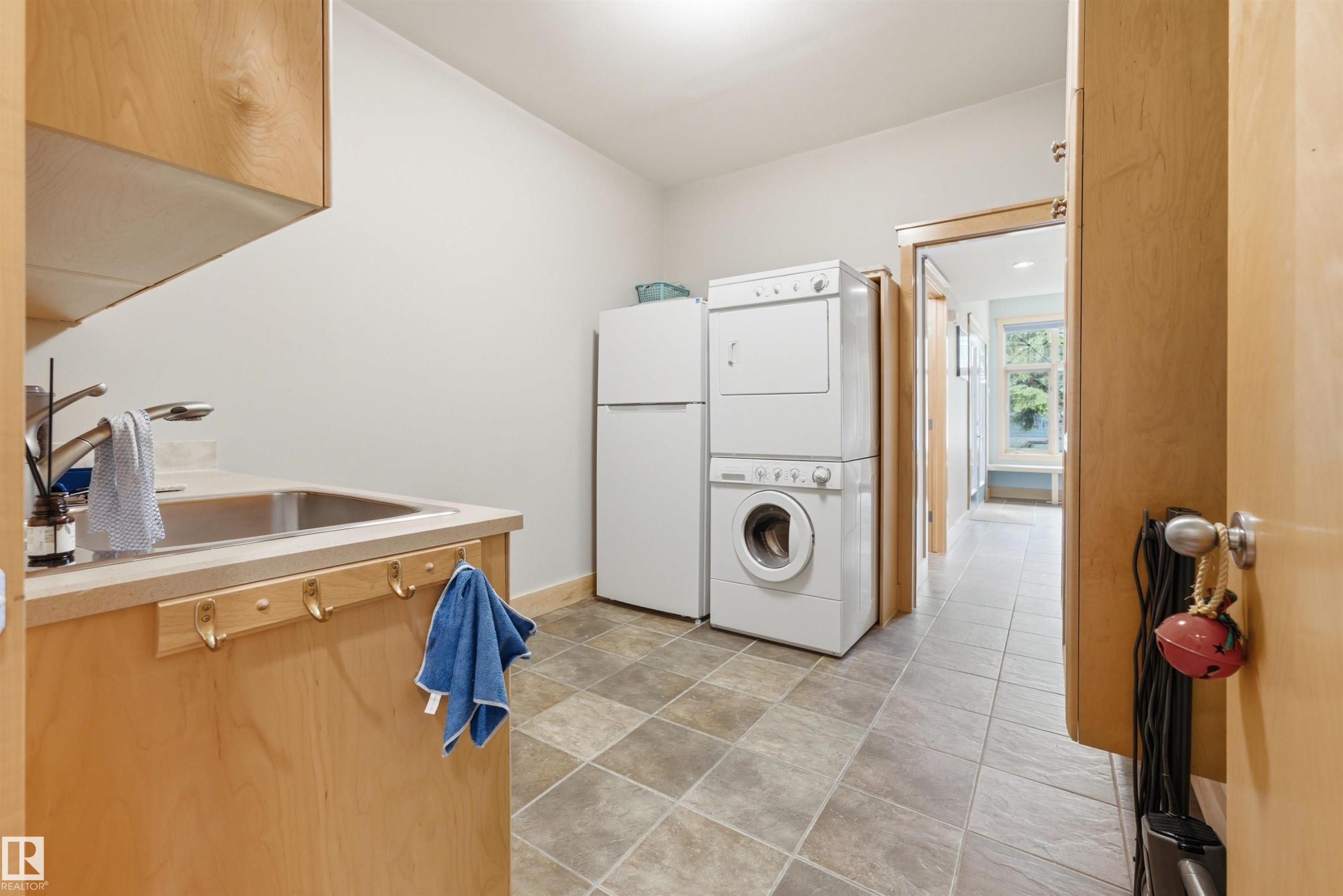 Utility room featuring light wood-finish cabinetry, a stainless steel undermount sink with a chrome faucet, and checkerboard floor tiling - A38 Bernice Ave, Rural Leduc County, AB