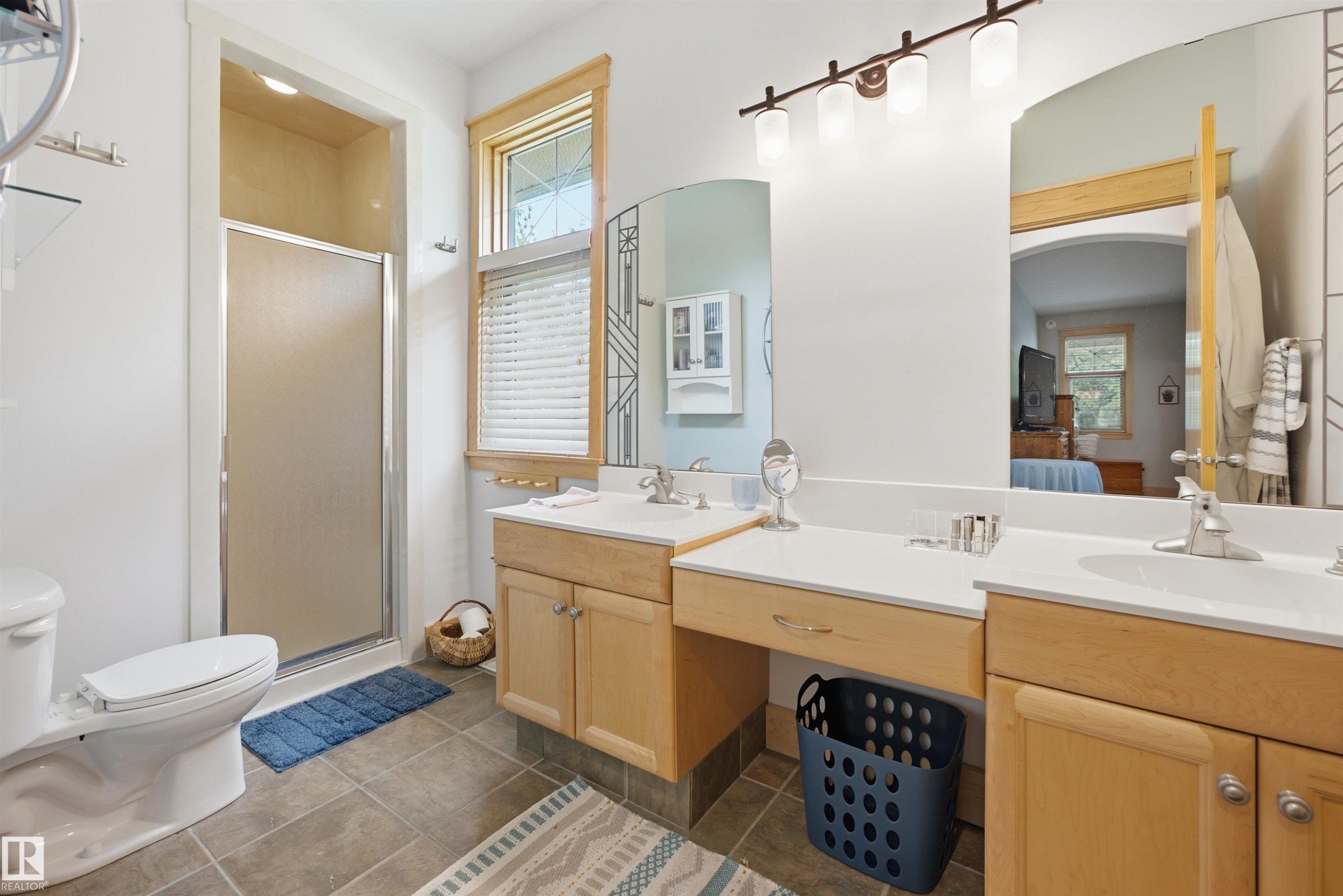 Bathroom featuring a glass-enclosed shower, dual vanities with integrated sinks, light wood cabinetry, and a window with blinds - A38 Bernice Ave, Rural Leduc County, AB
