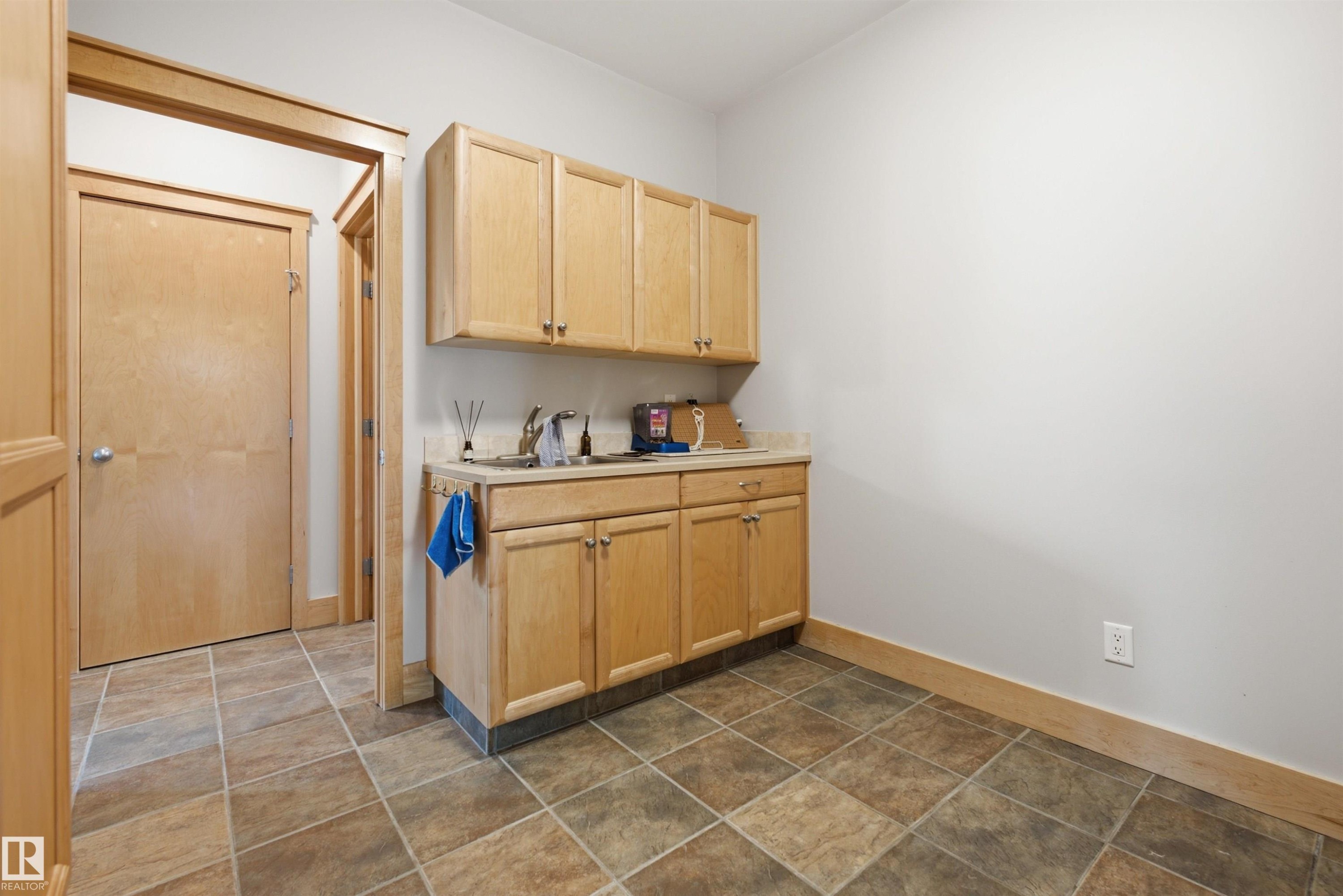 Utility room featuring a built-in light wood cabinetry with a sink, stainless steel faucet, and light-toned countertop - A38 Bernice Ave, Rural Leduc County, AB